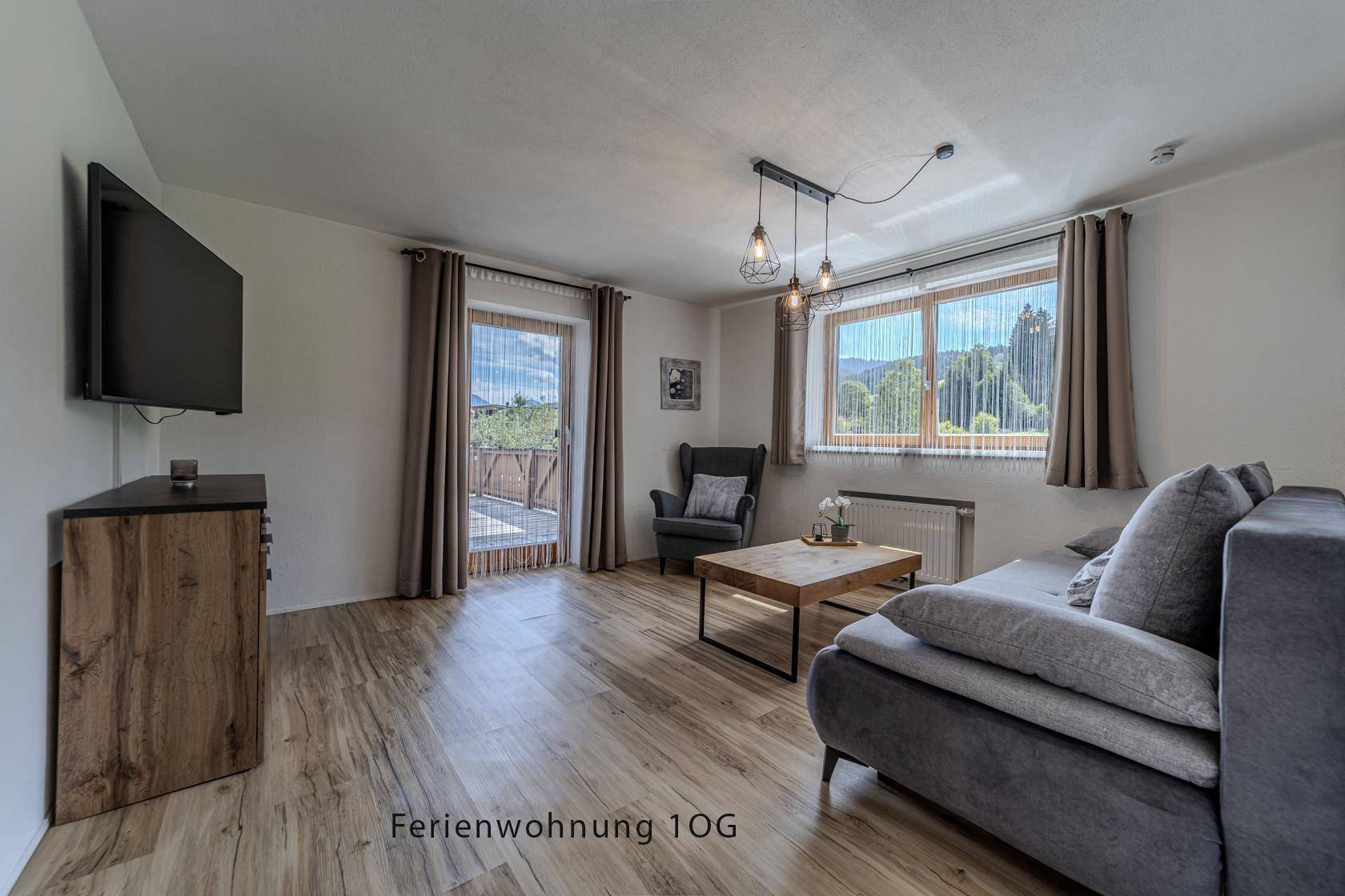 Gemütliches Wohnzimmer mit Sofa, Sessel und Zugang zu einem Balkon mit Bergblick.