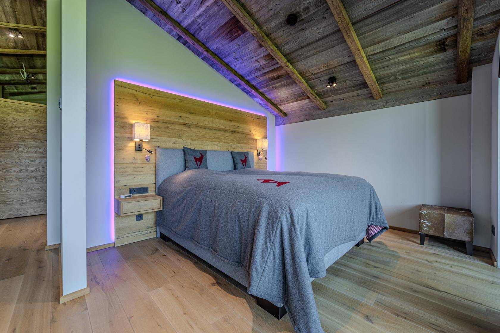 Modernes Schlafzimmer mit Holzakzentwand, indirekter Beleuchtung und rustikaler Holzbalkendecke.