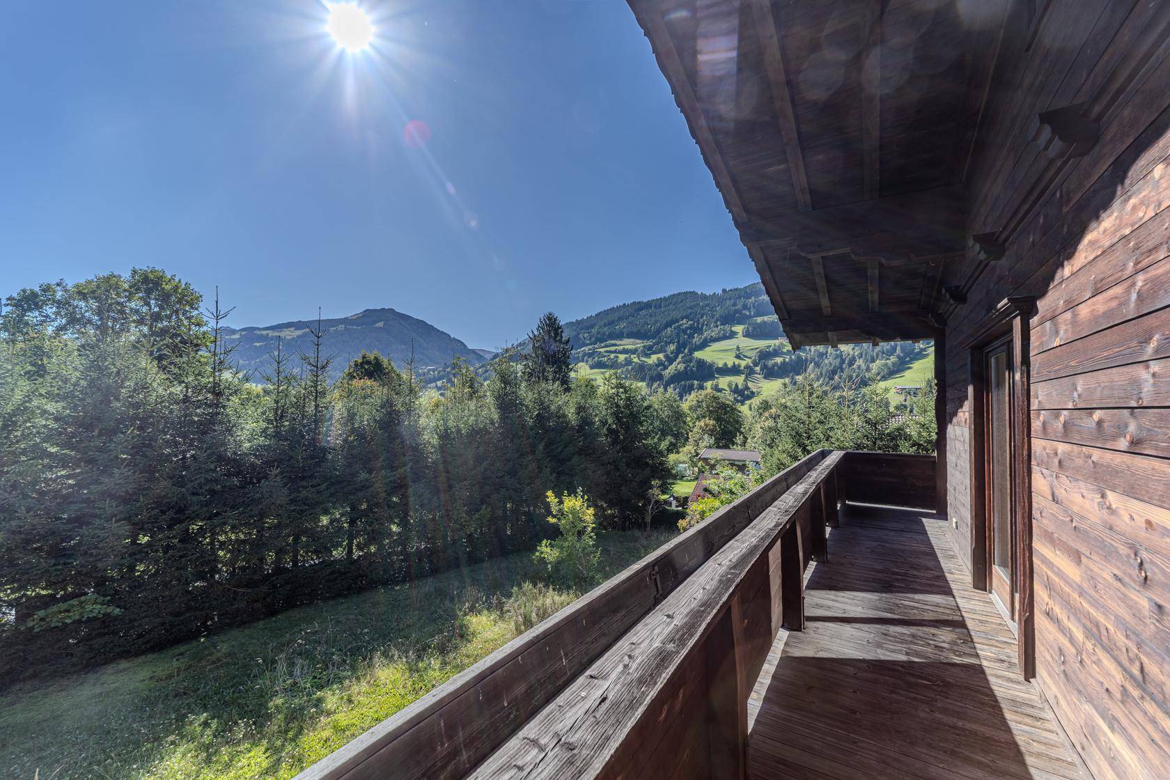 Geräumiger Holzbalkon mit weitem Blick auf die umliegenden grünen Berge und Wälder.