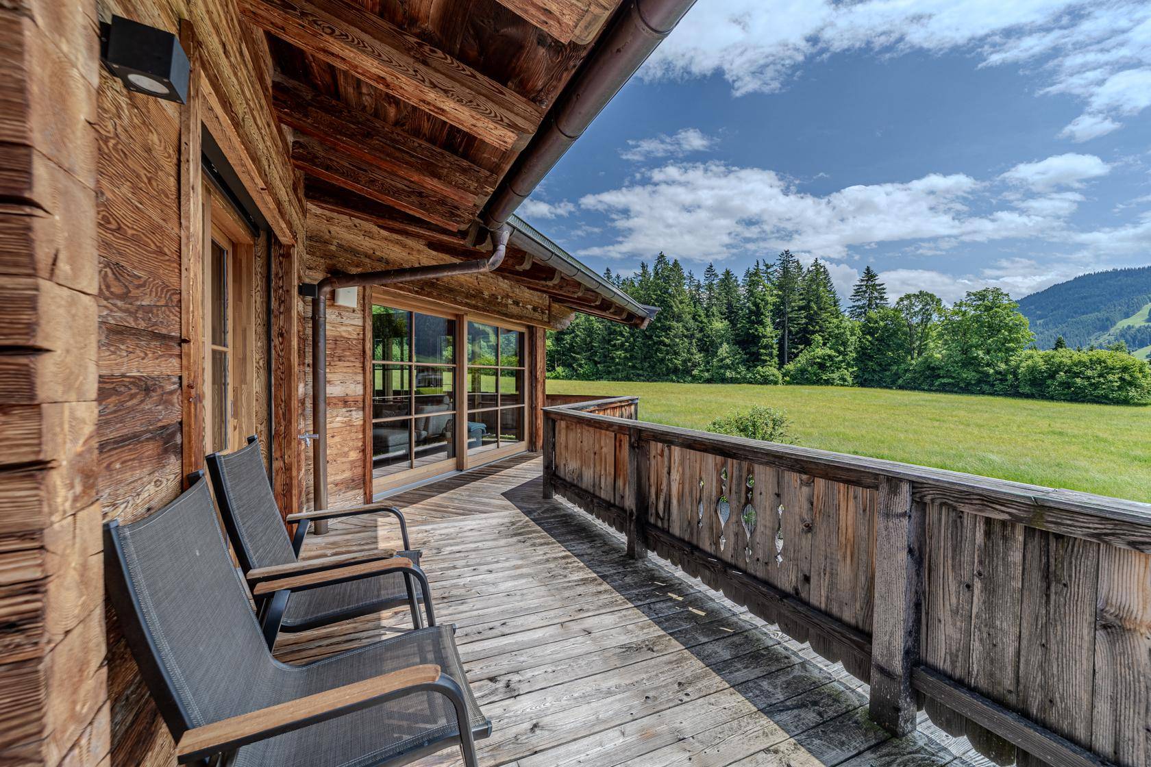 Holzbalkon mit Sitzgelegenheiten und weitem Blick über grüne Wiesen und Wälder.