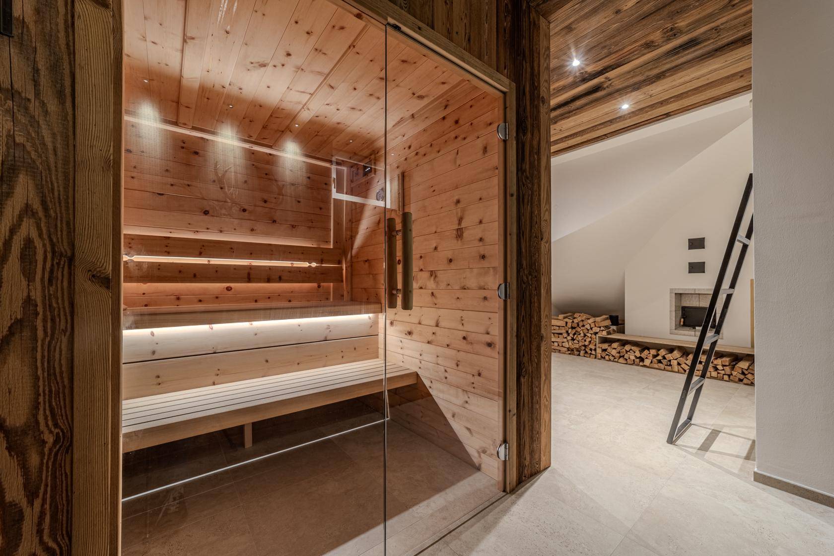 Private Sauna mit Holzverkleidung und Blick auf einen Bereich mit Kamin und Holzstapel.