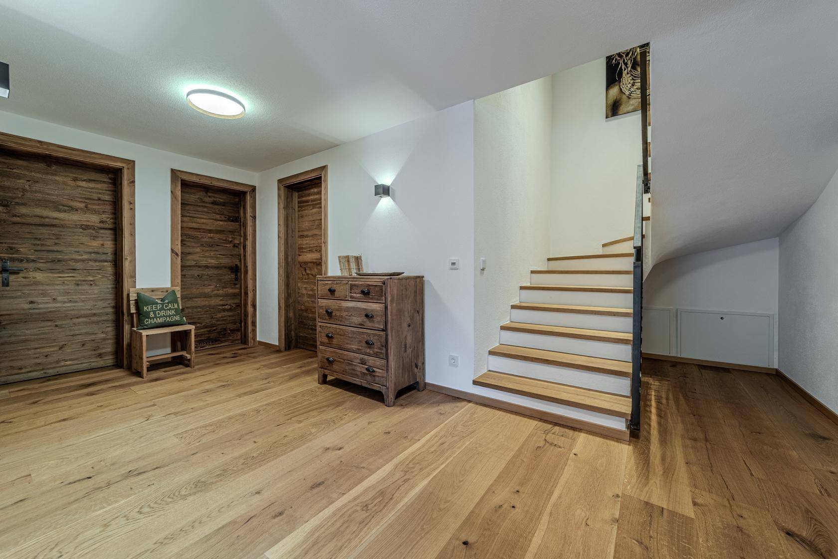 Heller Flur mit Holztüren, rustikaler Kommode und einer eleganten Holztreppe zum Obergeschoss.