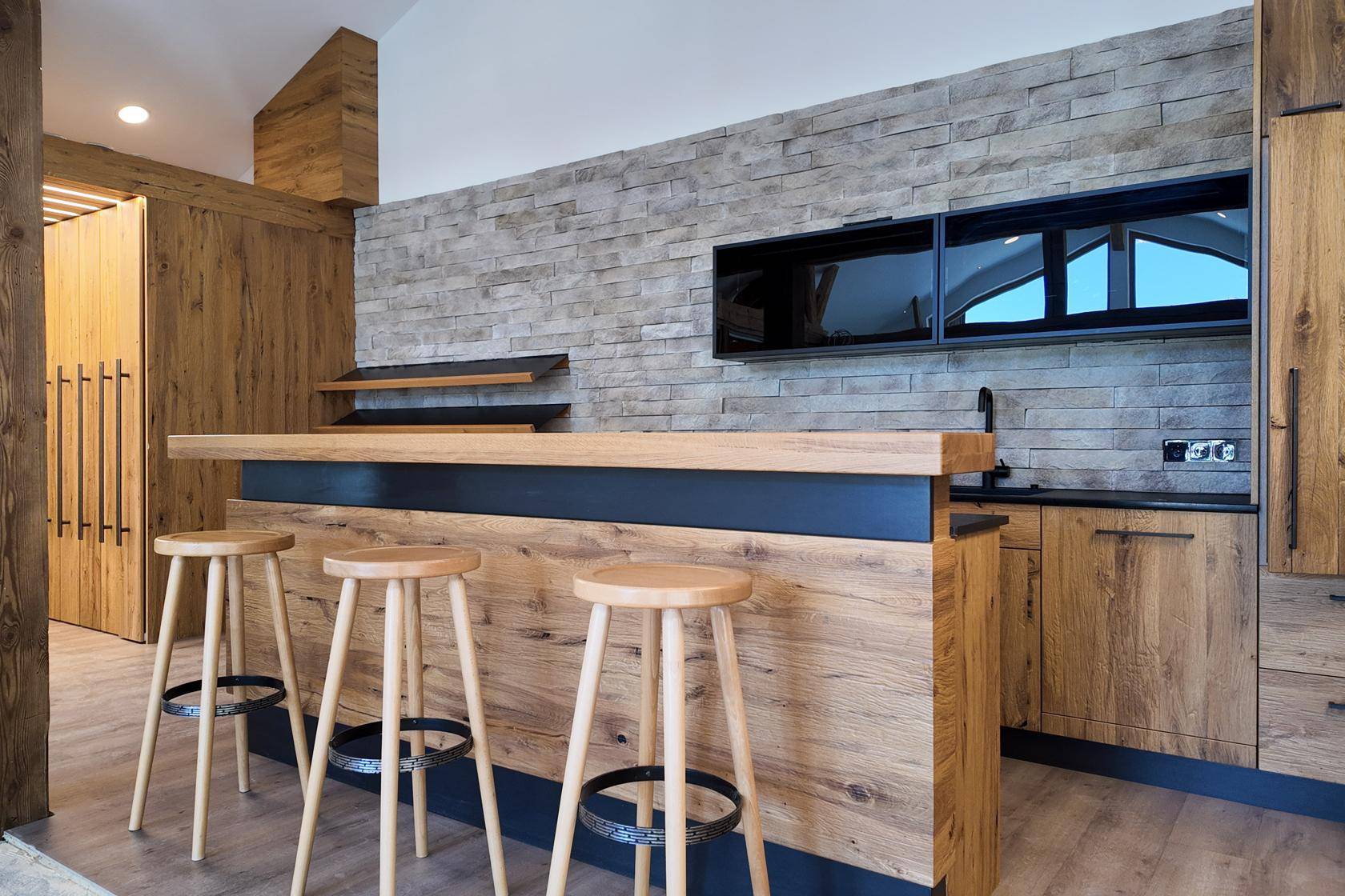 Moderne Küchenzeile mit Holzfronten, Steinwandverkleidung und einer Bar mit Hockern.