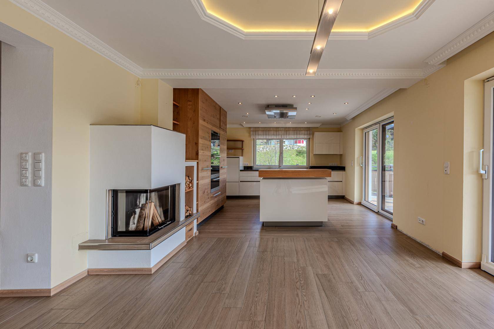 Lichtdurchfluteter Wohnbereich mit modernem Kamin, Holzboden und offener Küche mit Zugang nach draußen.