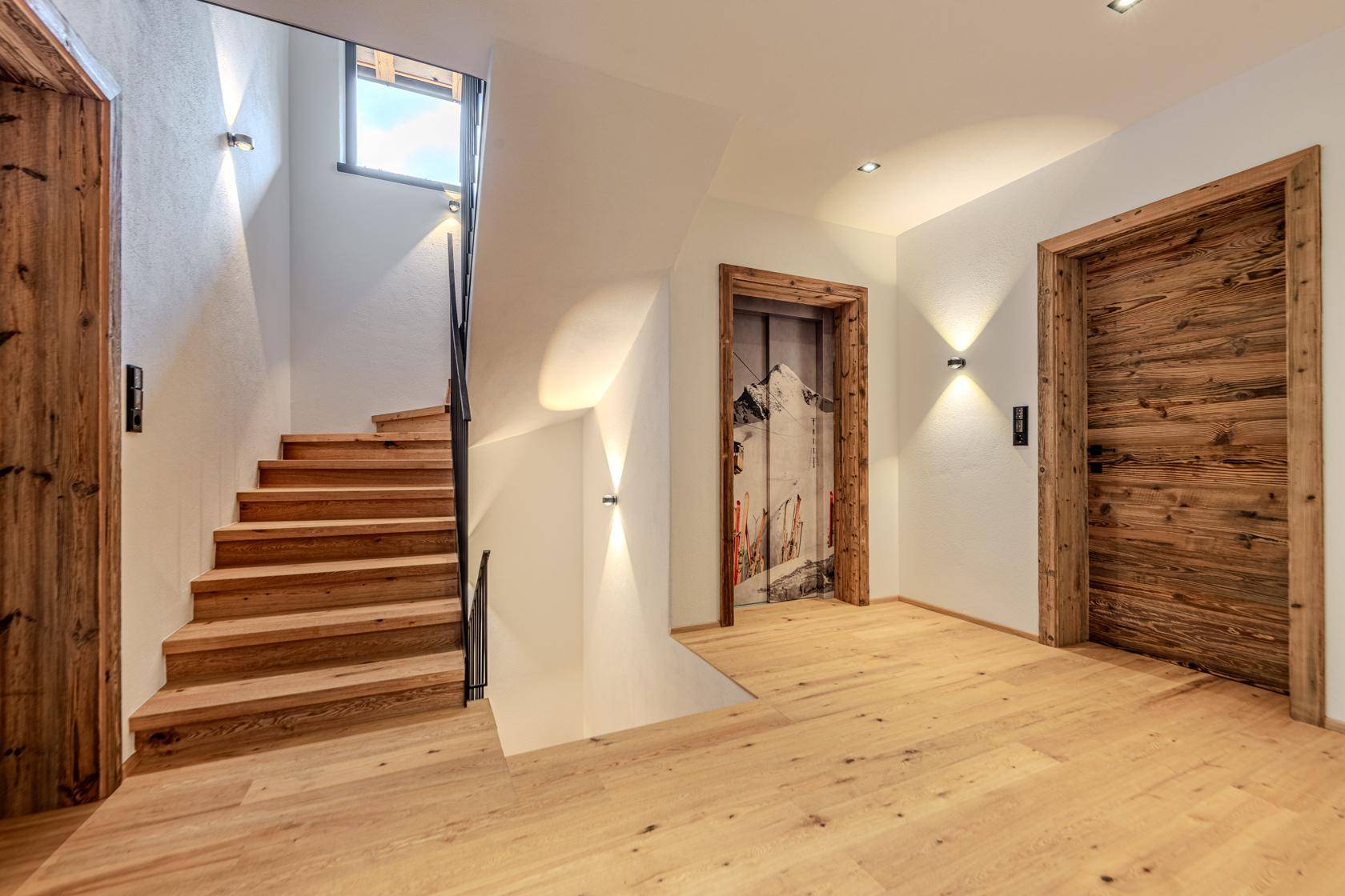 Heller Flur mit Holztreppe und Zugang zu einem modernen Aufzug.
