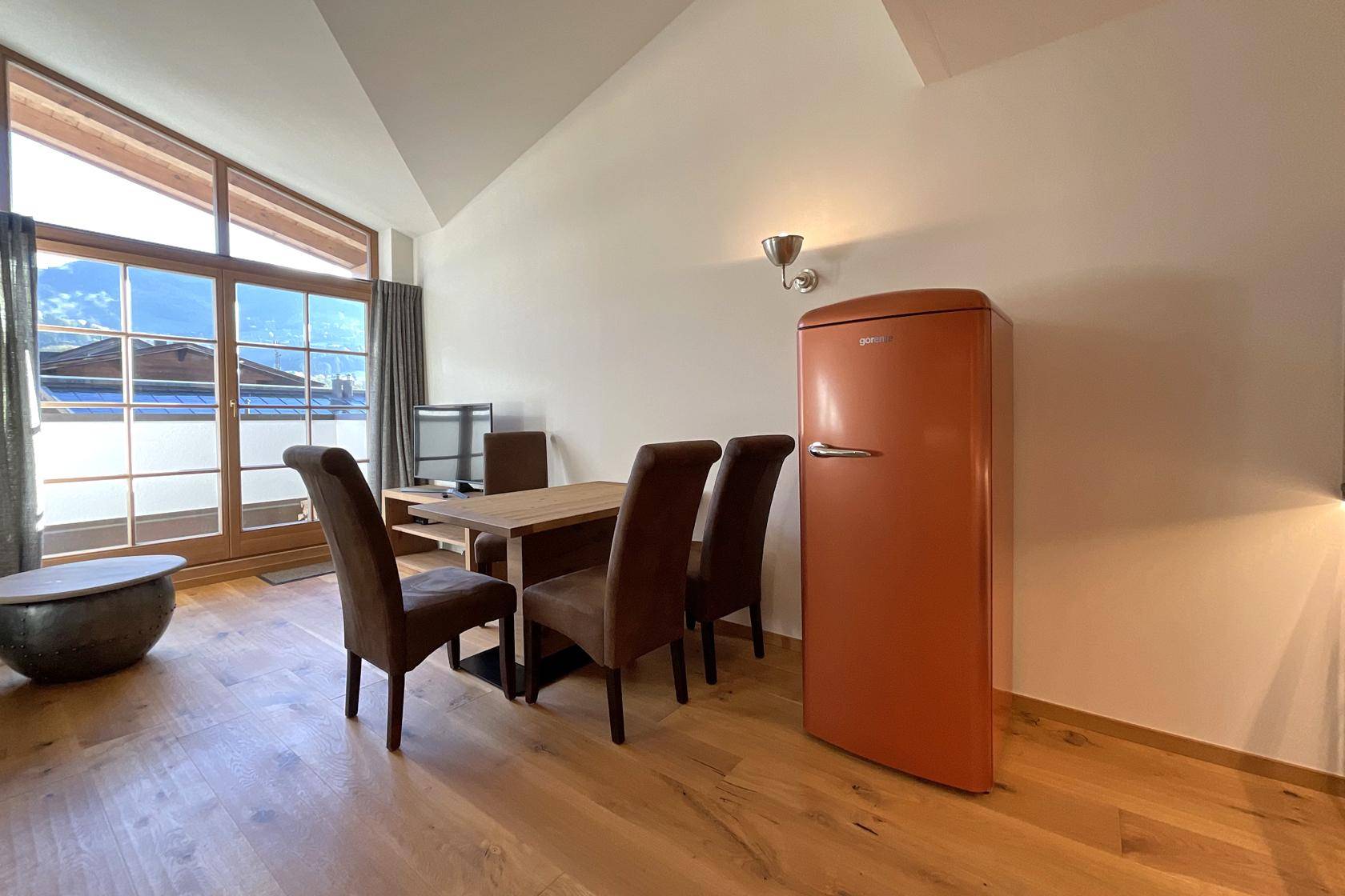 Heller Essbereich mit Holztisch, retro Kühlschrank und großen Fenstern mit Bergblick.