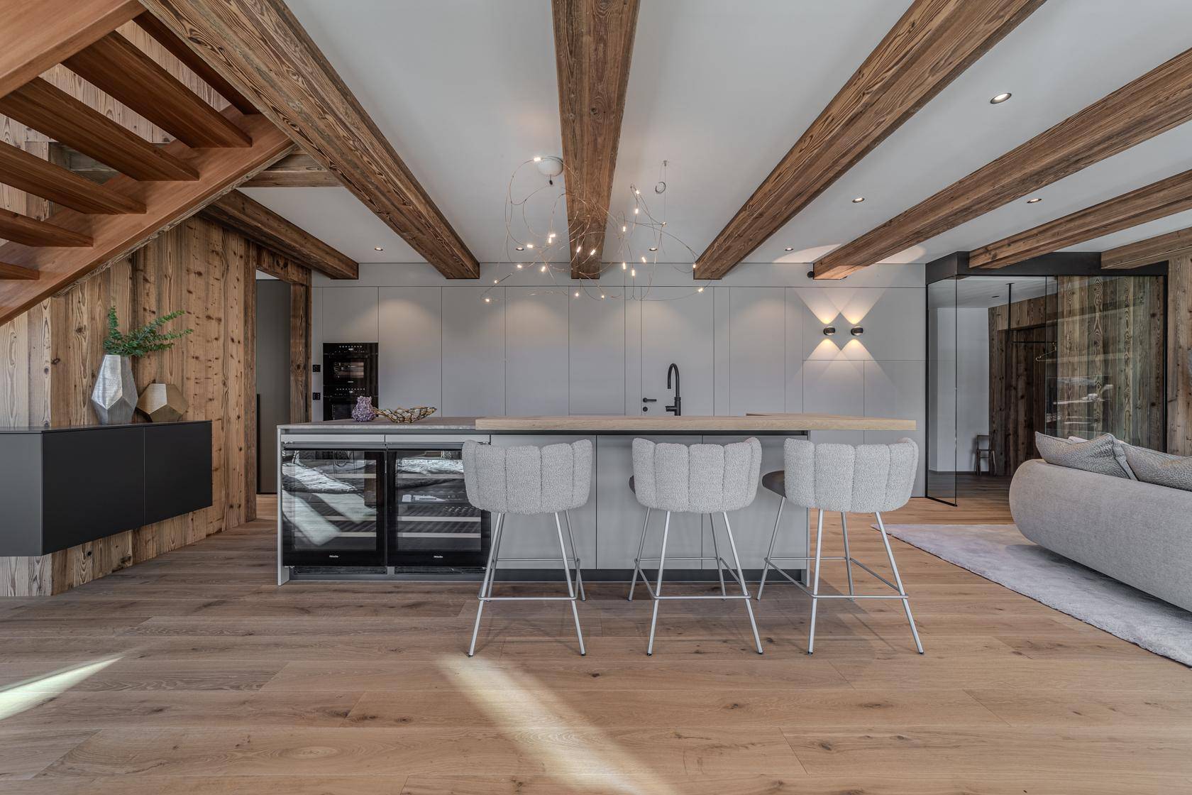 Moderne Küche mit Kücheninsel, Barhockern und integrierten Weinkühlern unter Holzbalken.