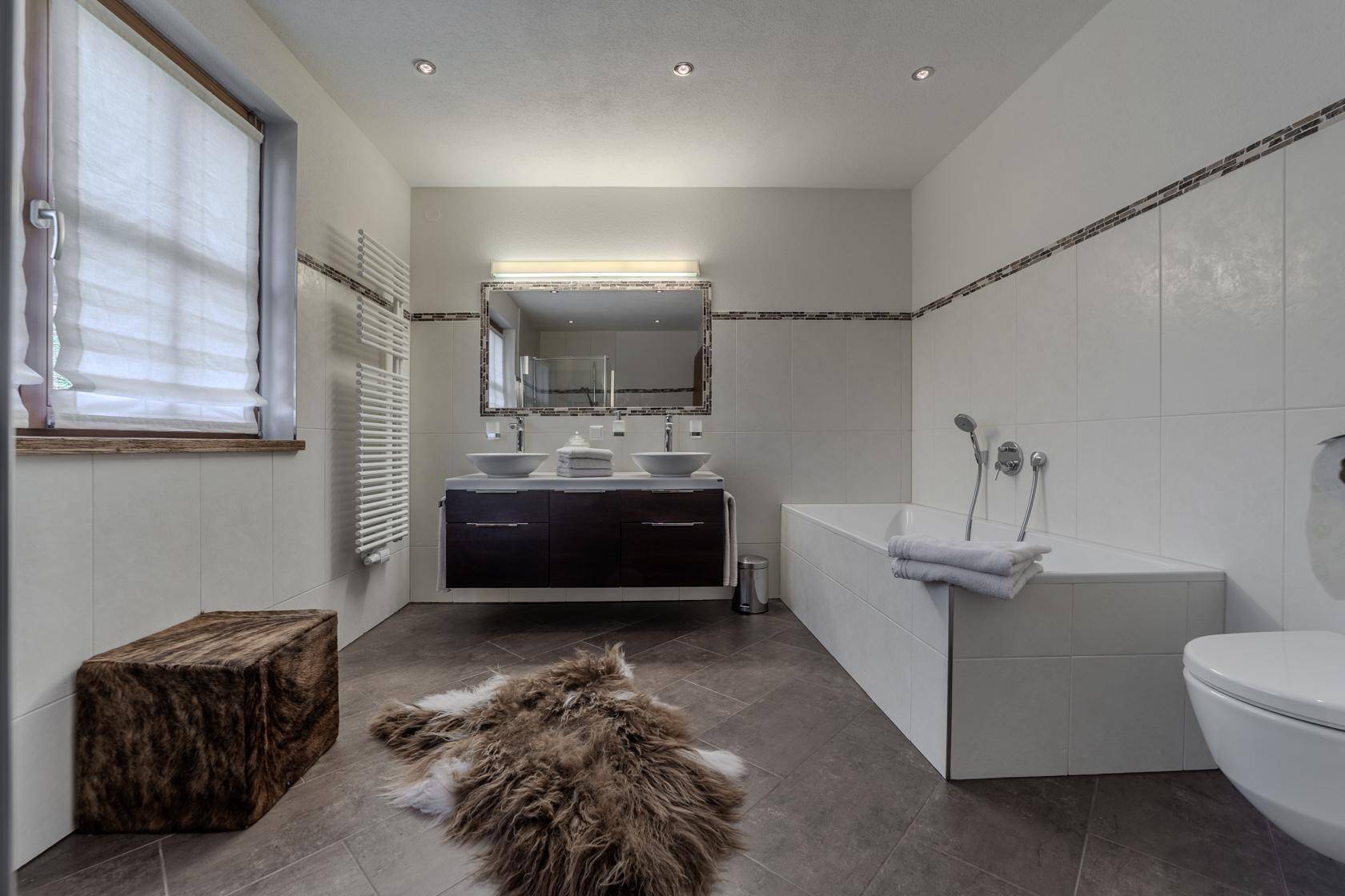 Helles Badezimmer mit Badewanne, Doppelwaschbecken und beheiztem Handtuchhalter.
