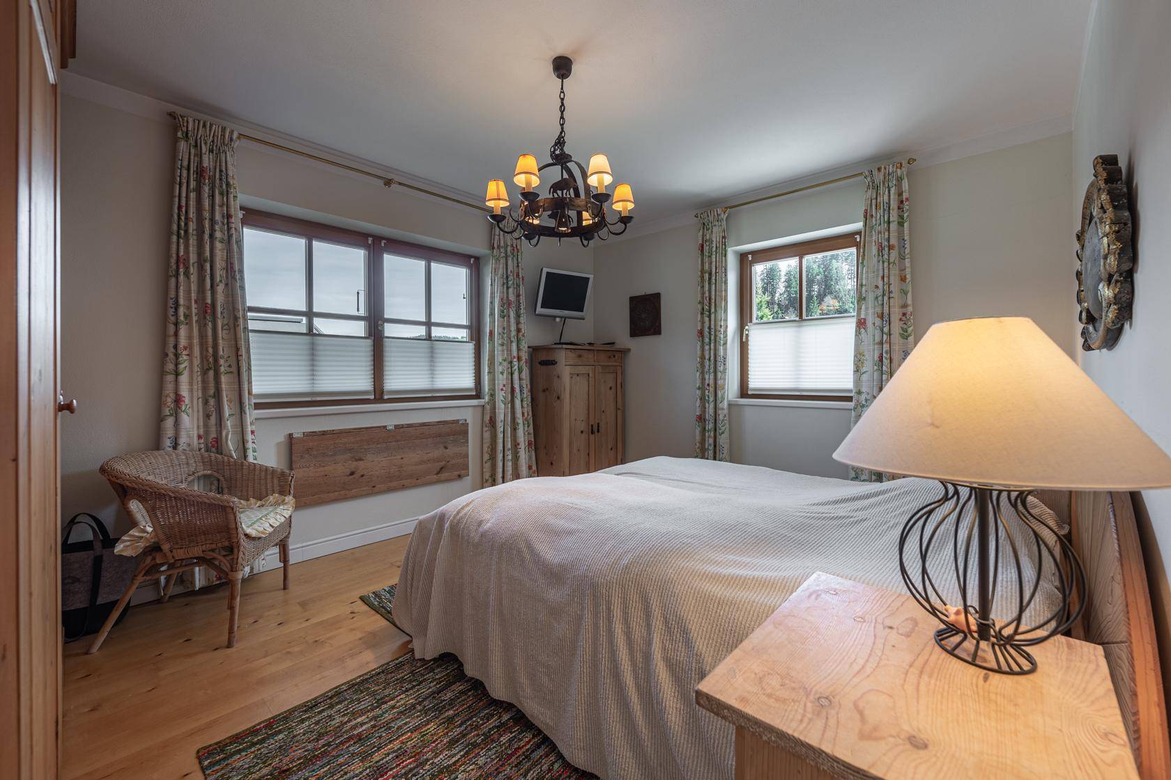 Helles Schlafzimmer mit Holzboden, zwei Fenstern und rustikalem Charme durch Holzdetails.