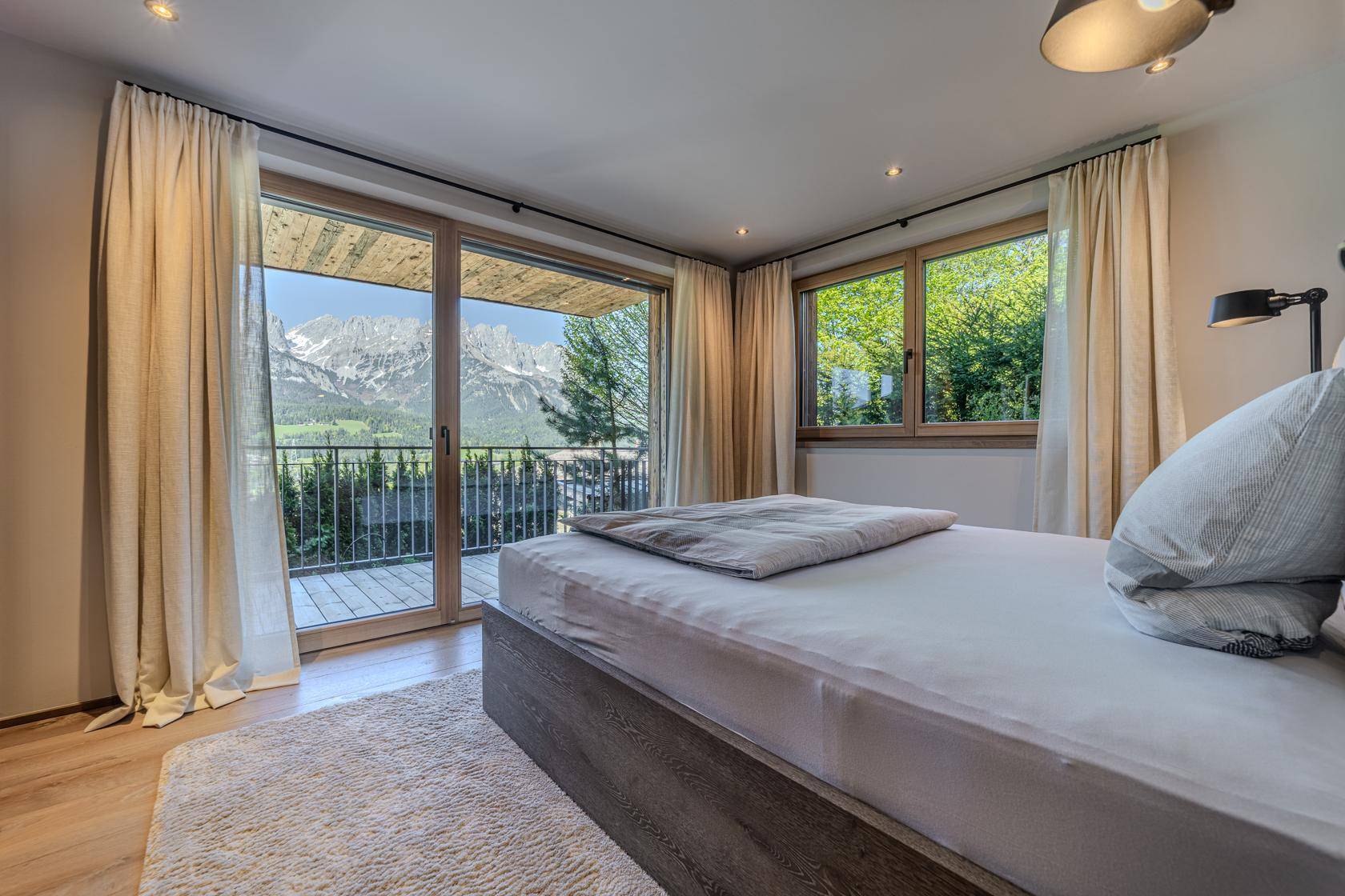 Helles Schlafzimmer mit Balkonzugang, Holzboden und weitem Blick auf die Bergwelt.
