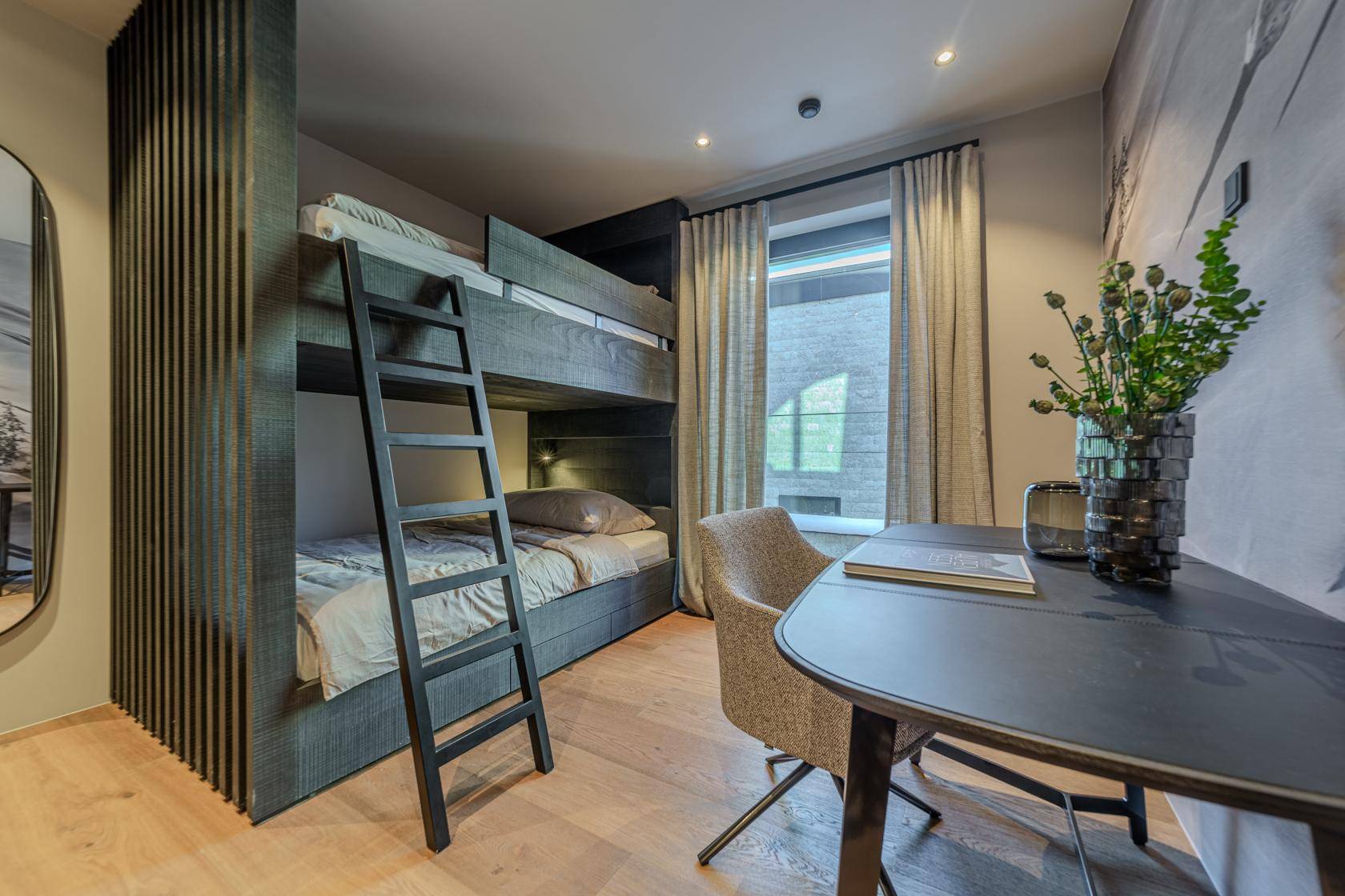 Gemütliches Schlafzimmer mit Etagenbetten, Holzboden und einem kleinen Schreibtischbereich.