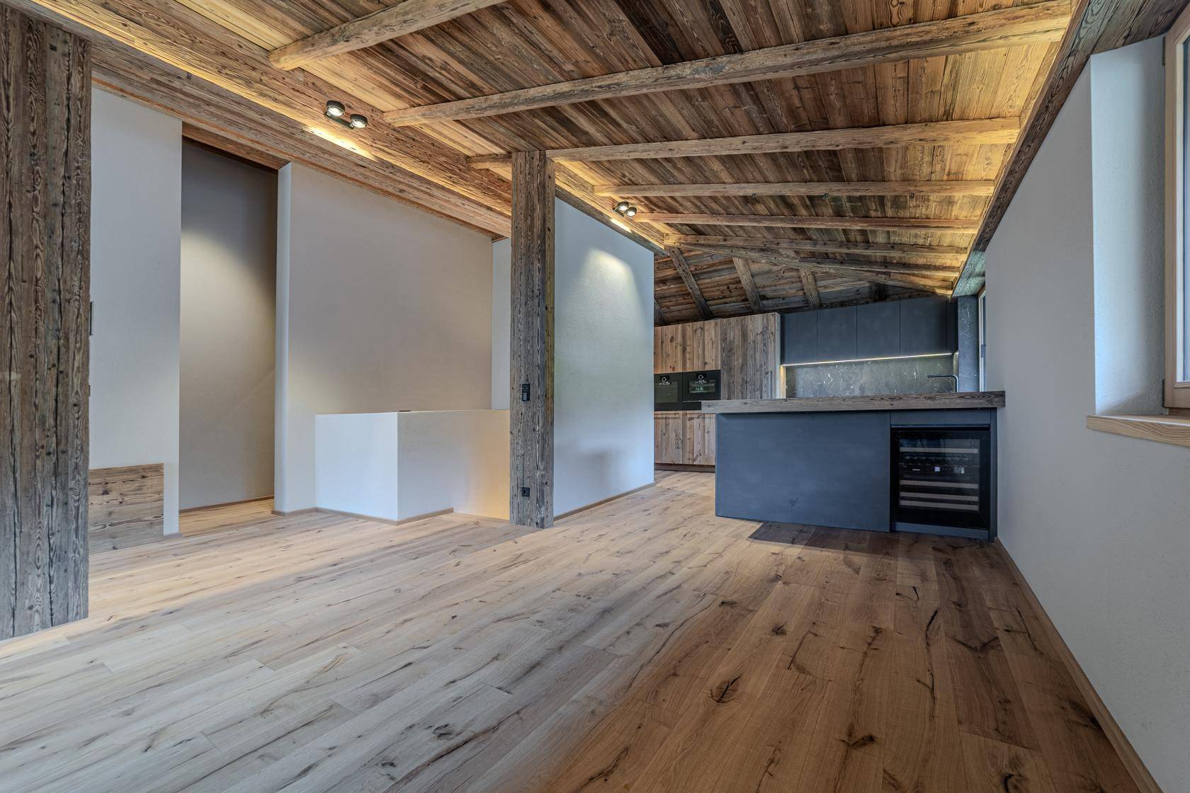 Geräumiger offener Wohnbereich mit Holzbalkendecke, Holzboden und integrierter moderner Küche mit Weinkühler.