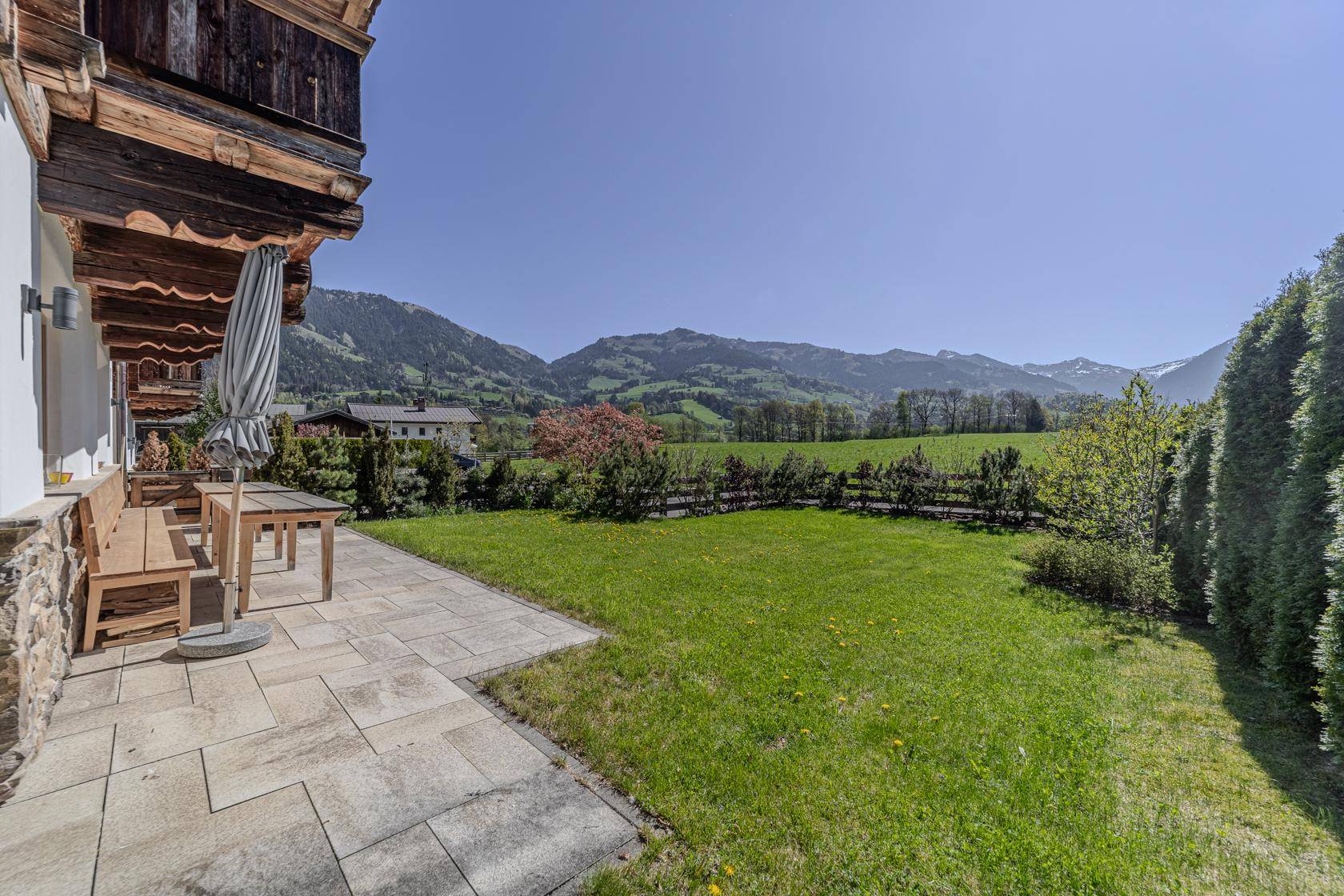 Sonnige Terrasse mit Gartenmöbeln, Rasenfläche und weitem Blick auf die Berglandschaft.