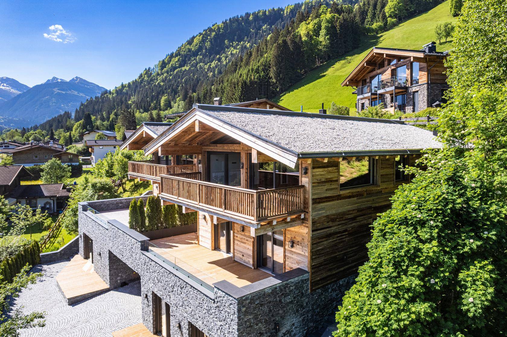 Luxuriöse Chalets in den Bergen mit Holzfassaden und Steinelementen, umgeben von grüner Natur.
