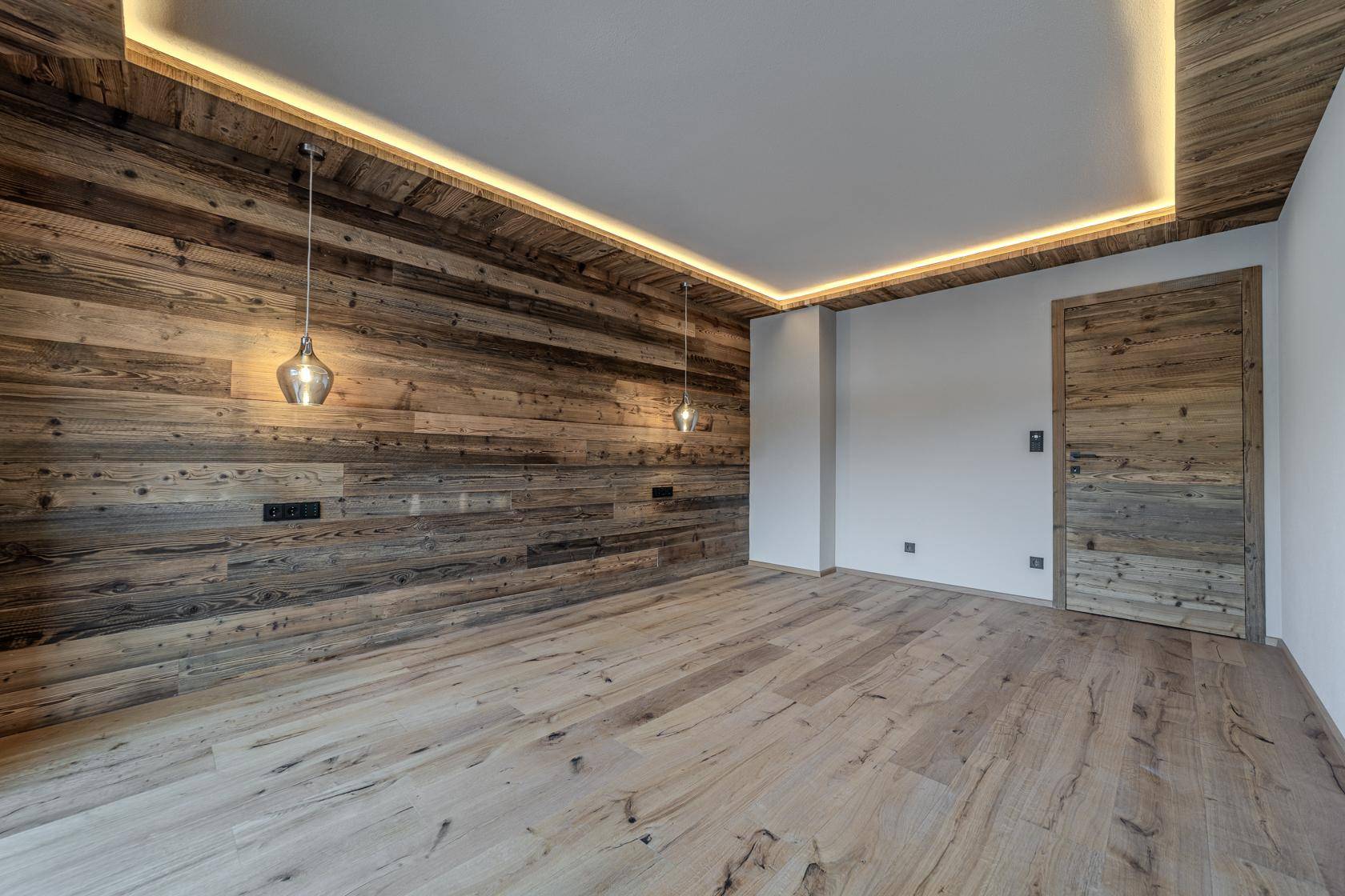 Gemütliches Schlafzimmer mit einer markanten Holzwand, indirekter Beleuchtung und hellem Holzboden.