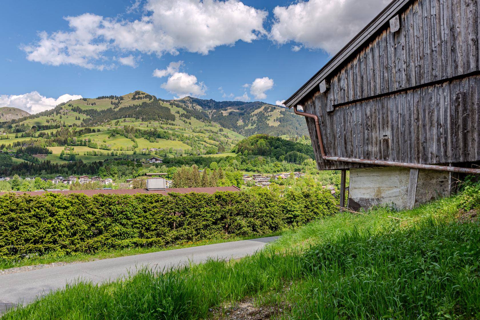 Rustikales Holzgebäude am Hang mit Blick auf die grüne Hügellandschaft und eine Hecke.
