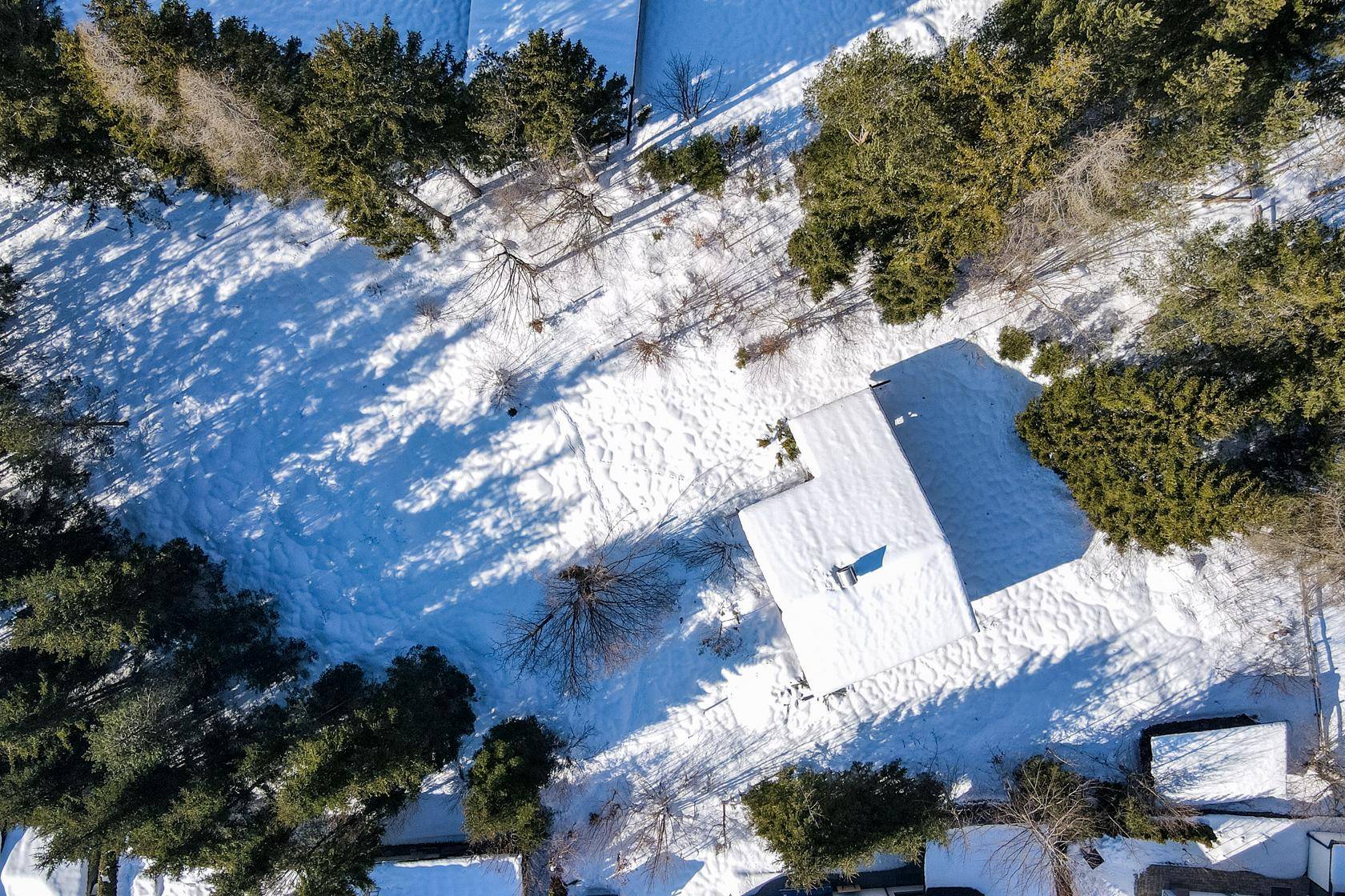 Luftaufnahme eines Hauses im Schnee, umgeben von Bäumen an einem sonnigen Wintertag.