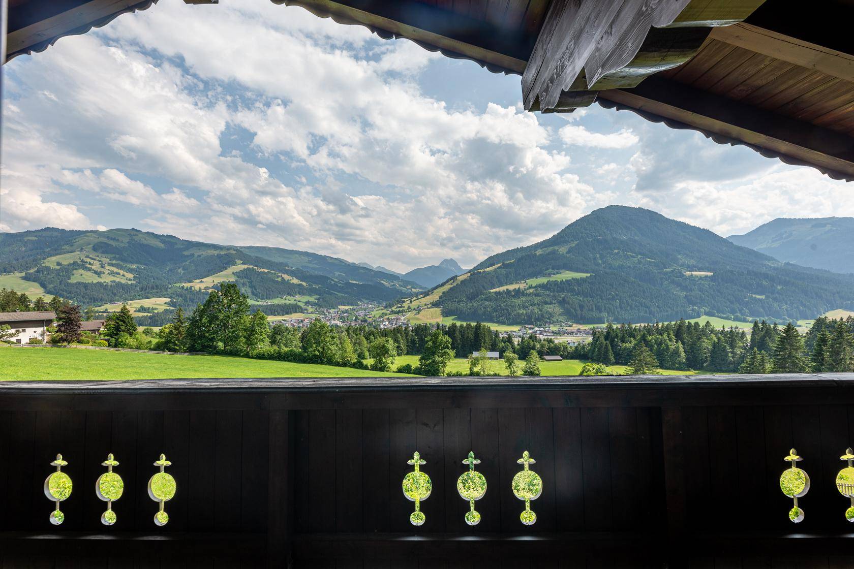Panoramablick vom Balkon über grüne Täler und majestätische Berge unter blauem Himmel.