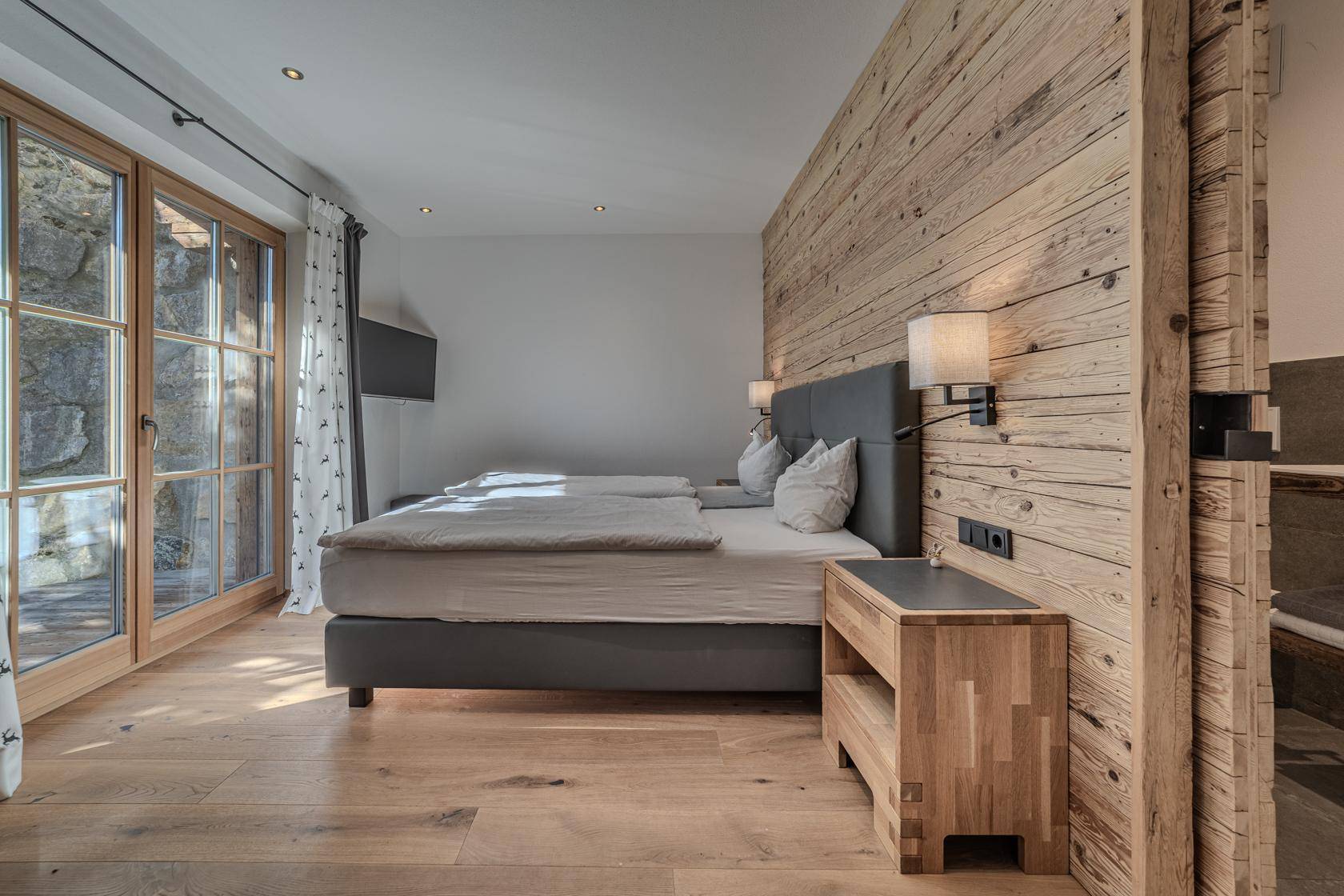Schlafzimmer mit Holzwand, Zugang zur Terrasse und Blick ins Grüne.
