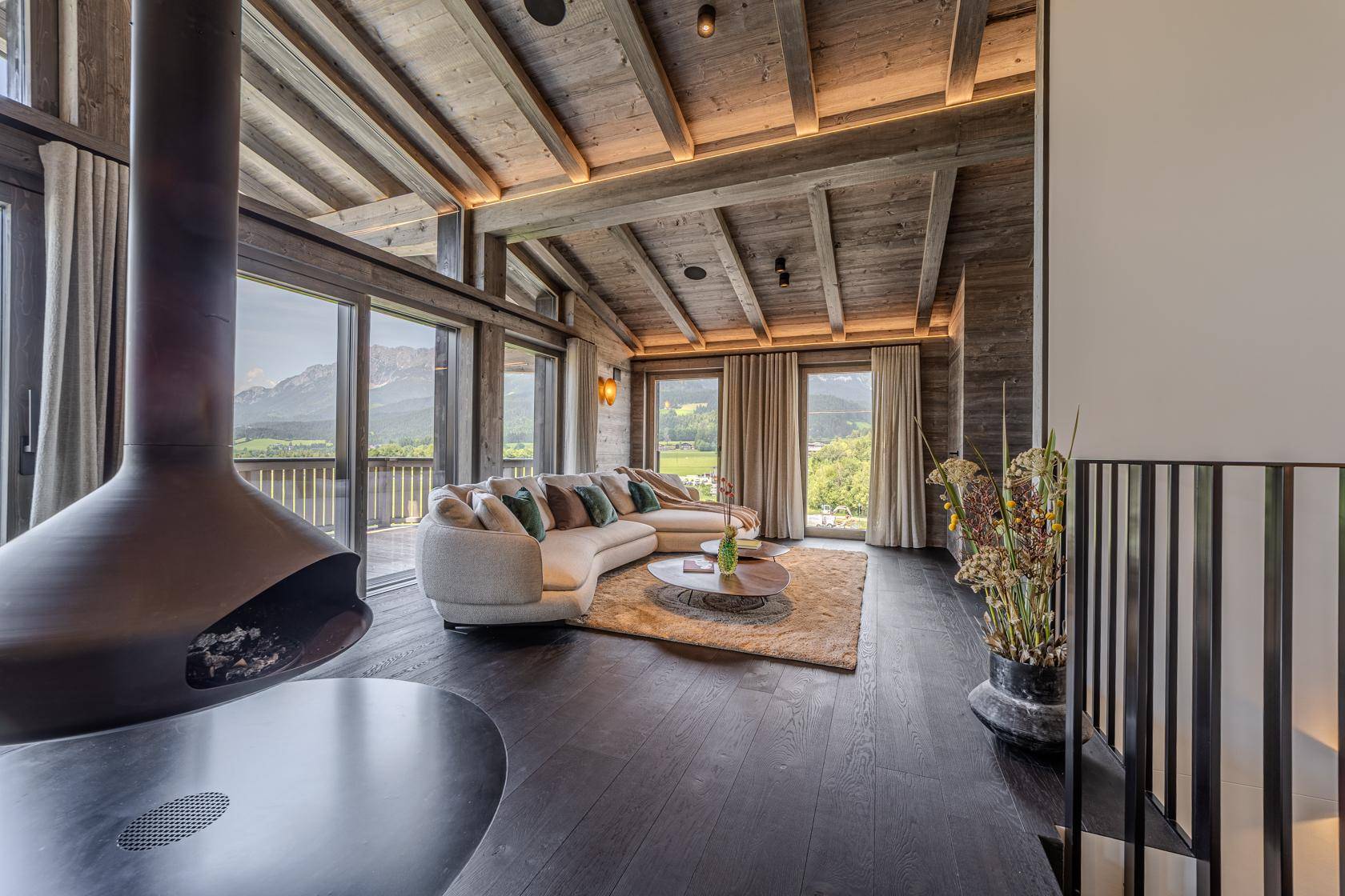Gemütlicher Wohnbereich mit modernem Hängekamin, bequemer Couch und weitem Blick auf die Berge.