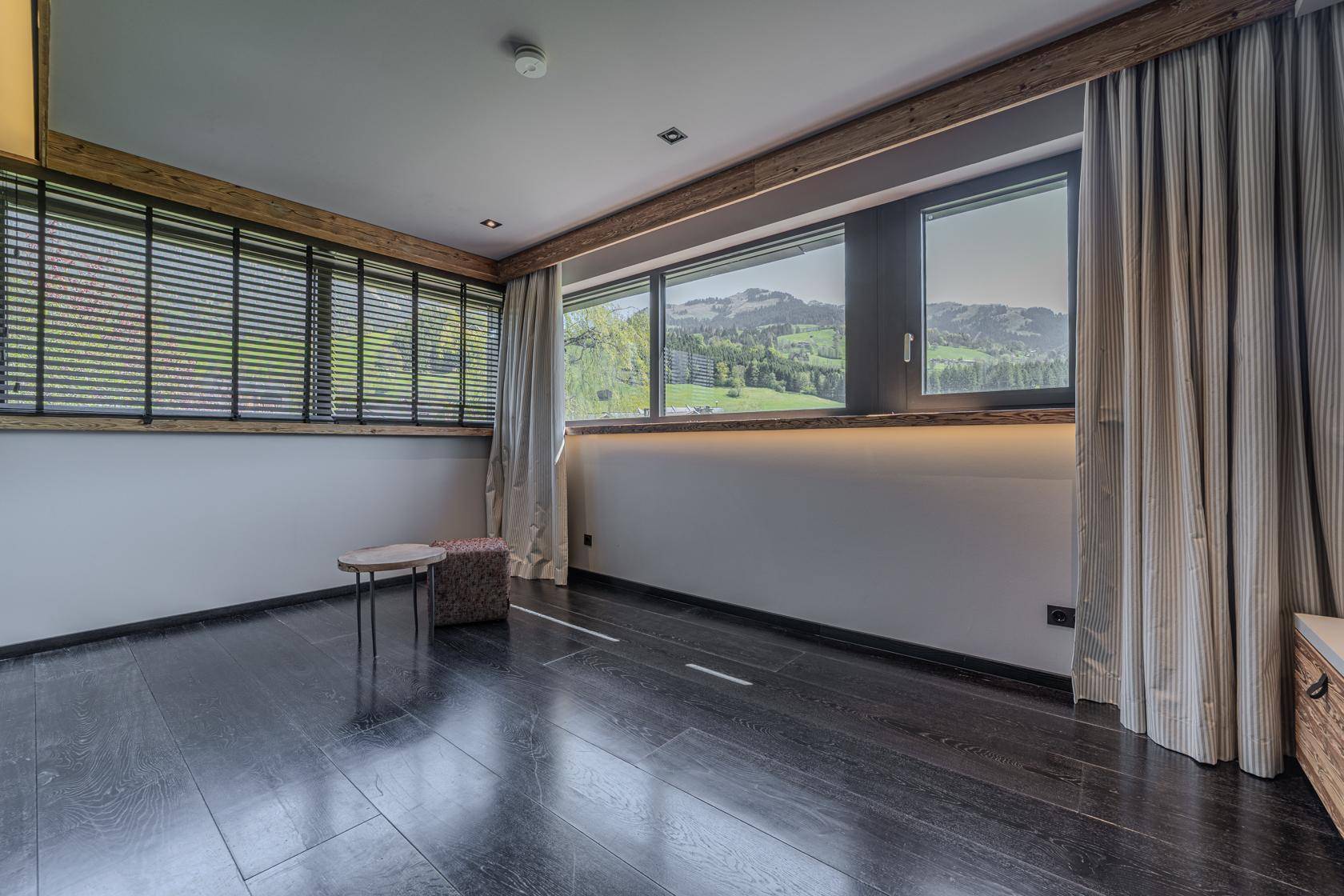 Helles Zimmer mit dunklem Holzboden und großen Fenstern, die einen weiten Blick auf die Landschaft bieten.