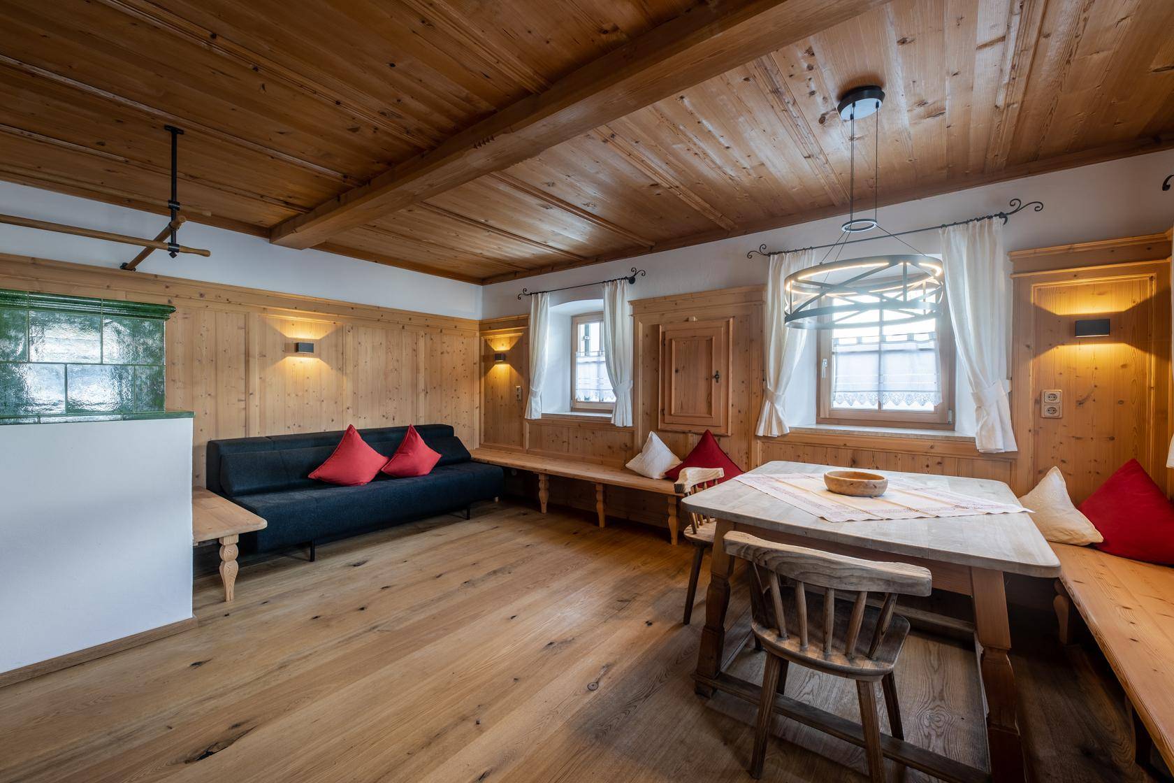 Gemütliches Wohnzimmer mit Holzboden, Kachelofen und traditionellen Holzvertäfelungen.
