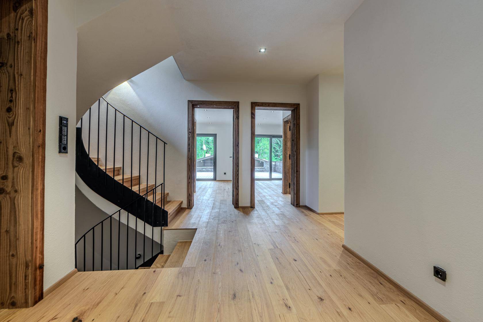Heller Flur mit geschwungener Holztreppe und Holzboden, der zu weiteren Räumen führt.