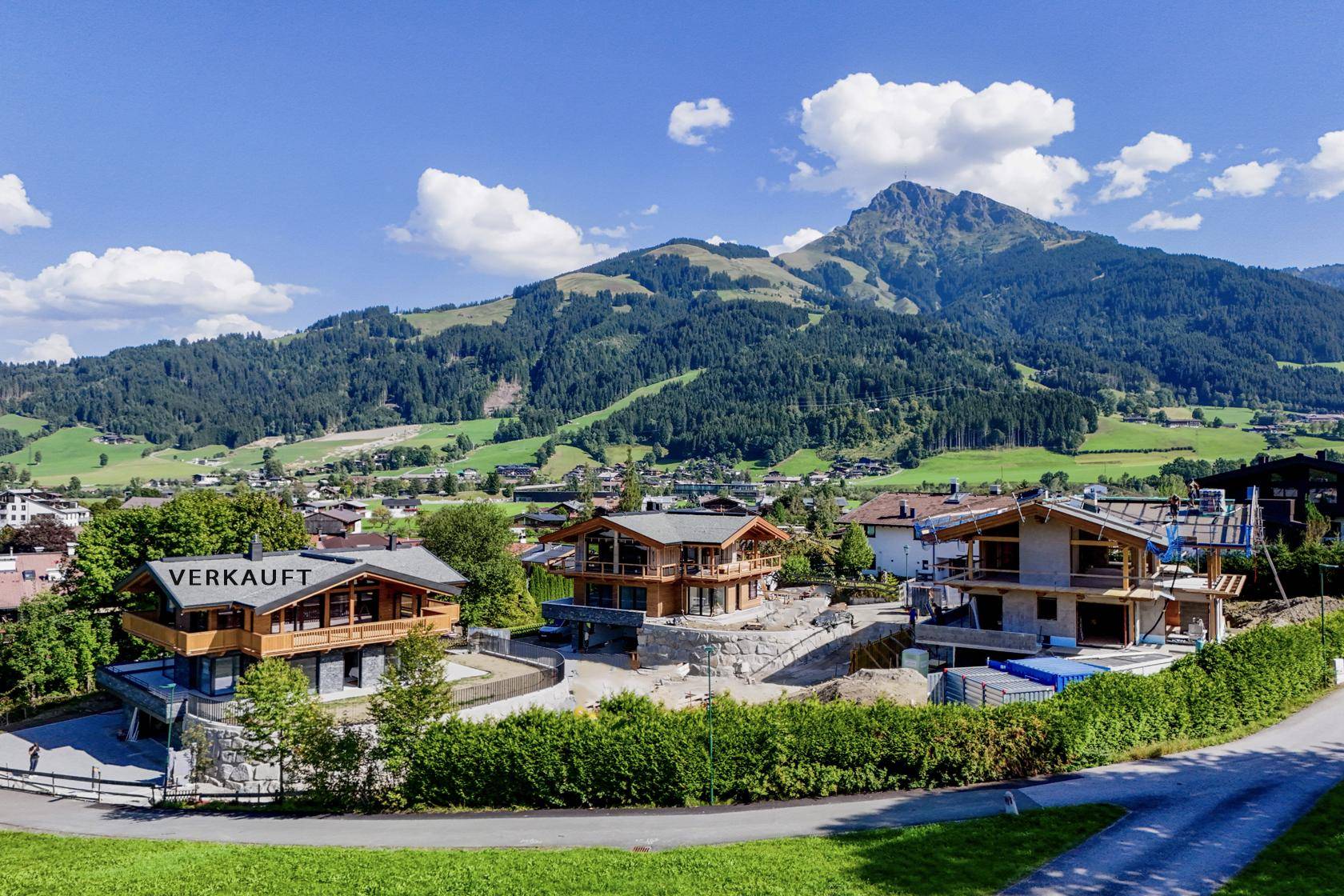 Luftaufnahme von mehreren Chalets in einer grünen Berglandschaft mit dem Hinweis "VERKAUFT".