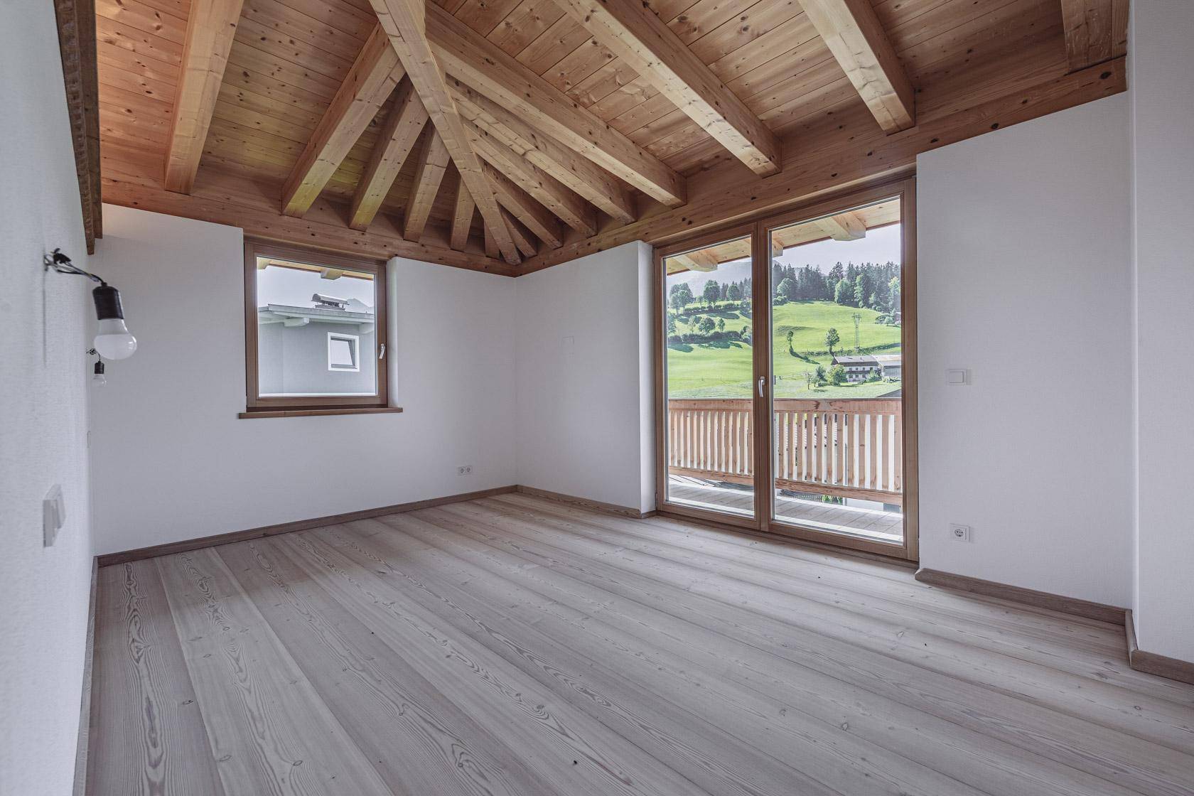 Helles Zimmer mit Holzbalkendecke, Holzboden und Zugang zum Balkon mit Bergblick.