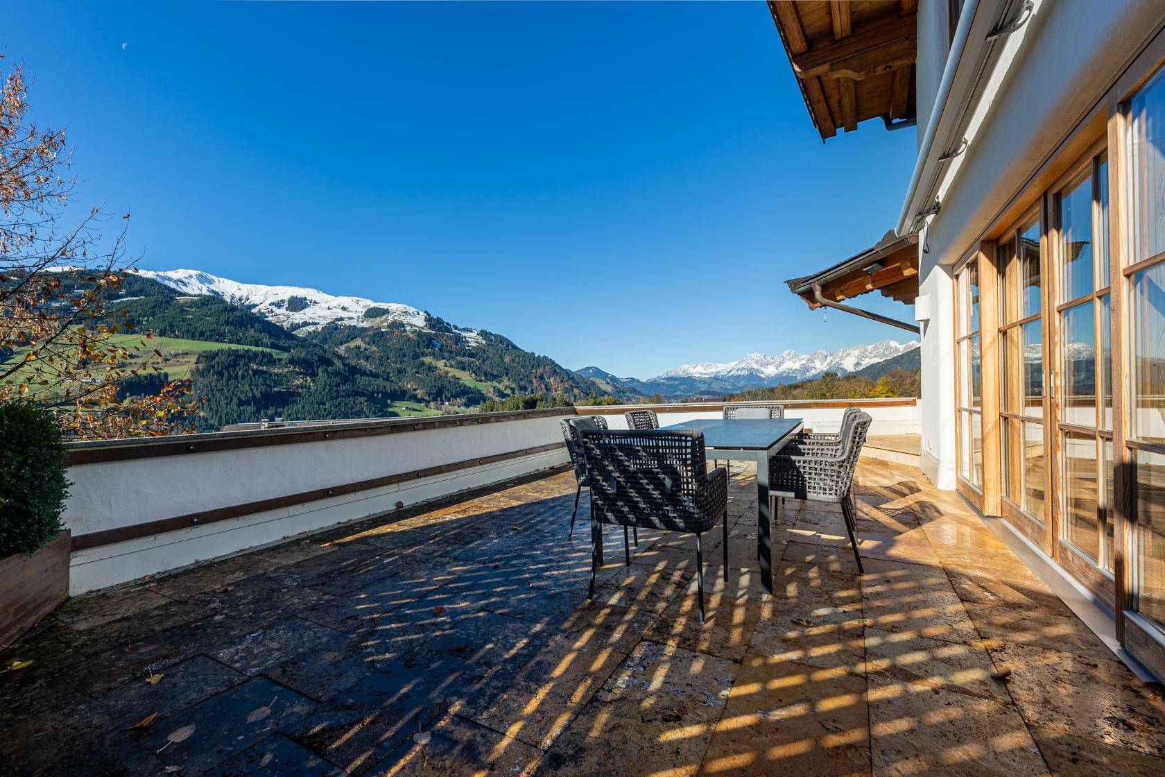 Sonnige Terrasse mit Steinfliesen und Sitzgelegenheiten bietet einen weiten Blick auf die schneebedeckten Berge.