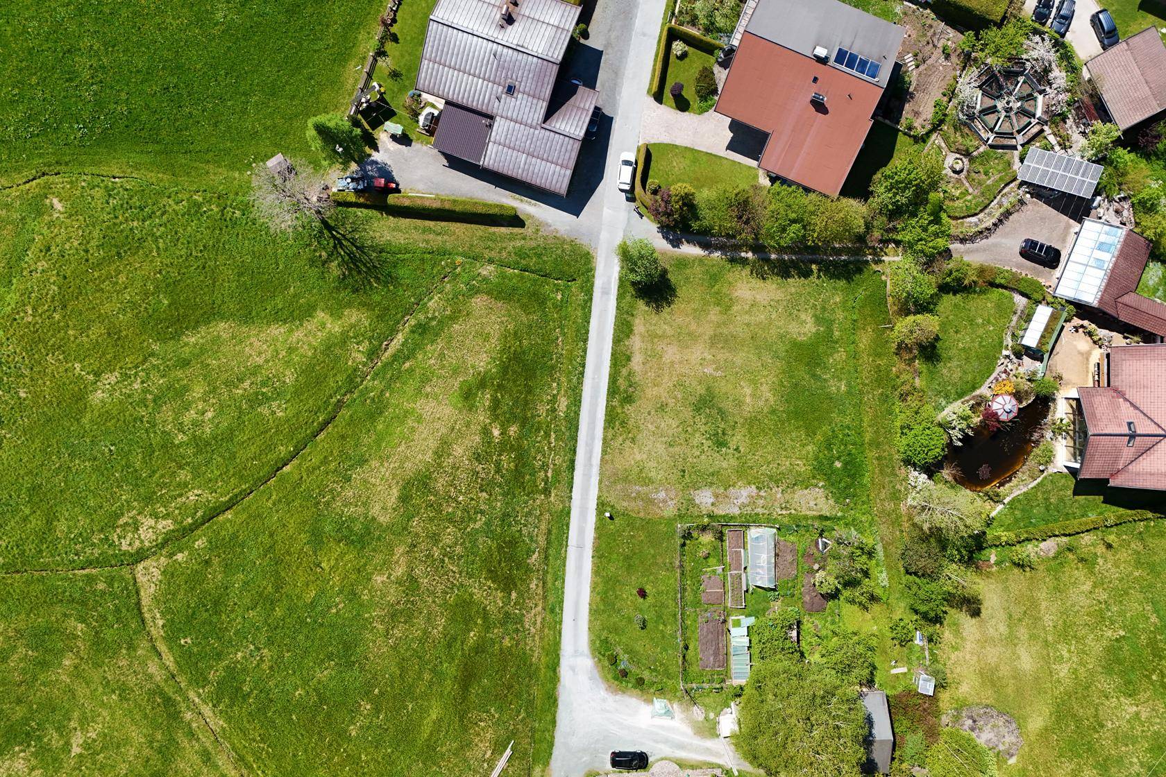Draufsicht auf ein Wohngebiet mit Häusern, Gärten und einer Zufahrtsstraße in ländlicher Umgebung.