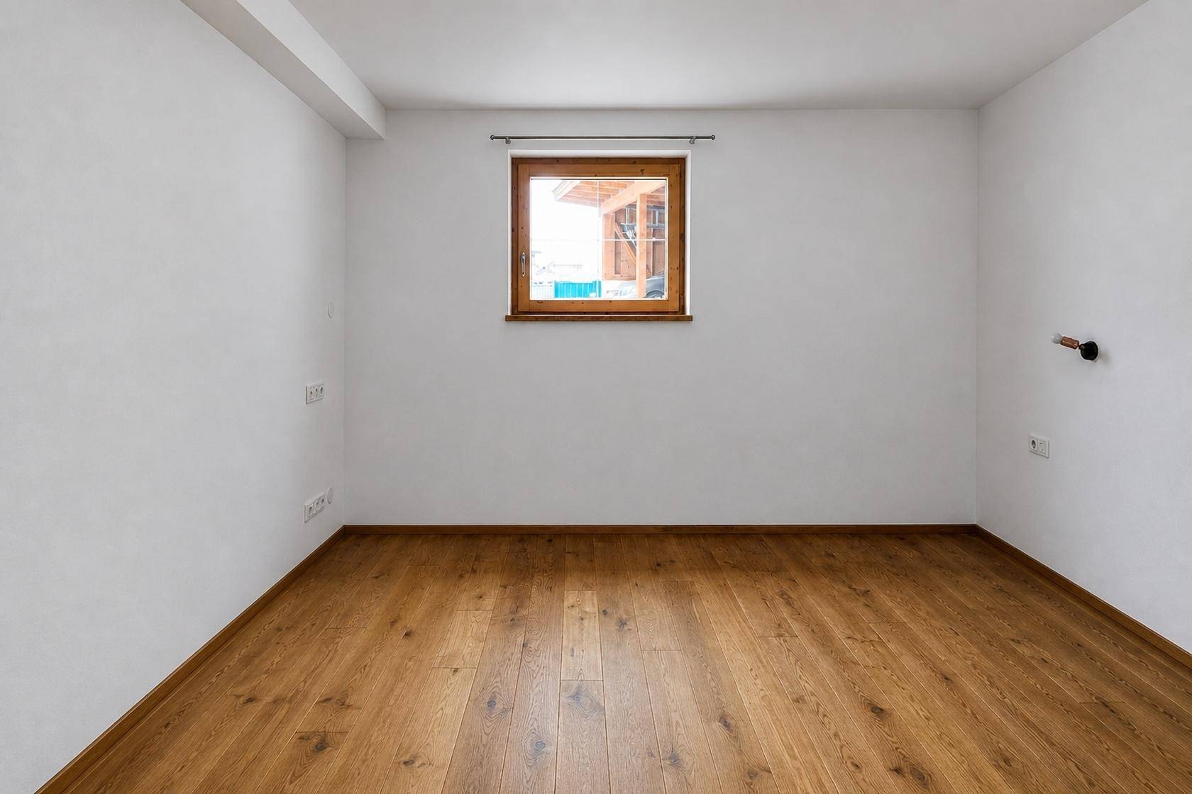 Leeres Schlafzimmer mit Holzboden und einem Fenster, das für natürliche Belichtung sorgt.