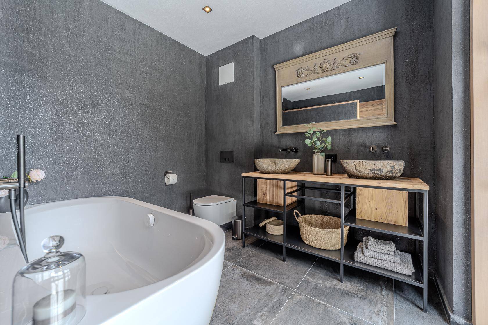Luxuriöses Badezimmer mit freistehender Badewanne, Doppelwaschbecken und dunklen Fliesen.