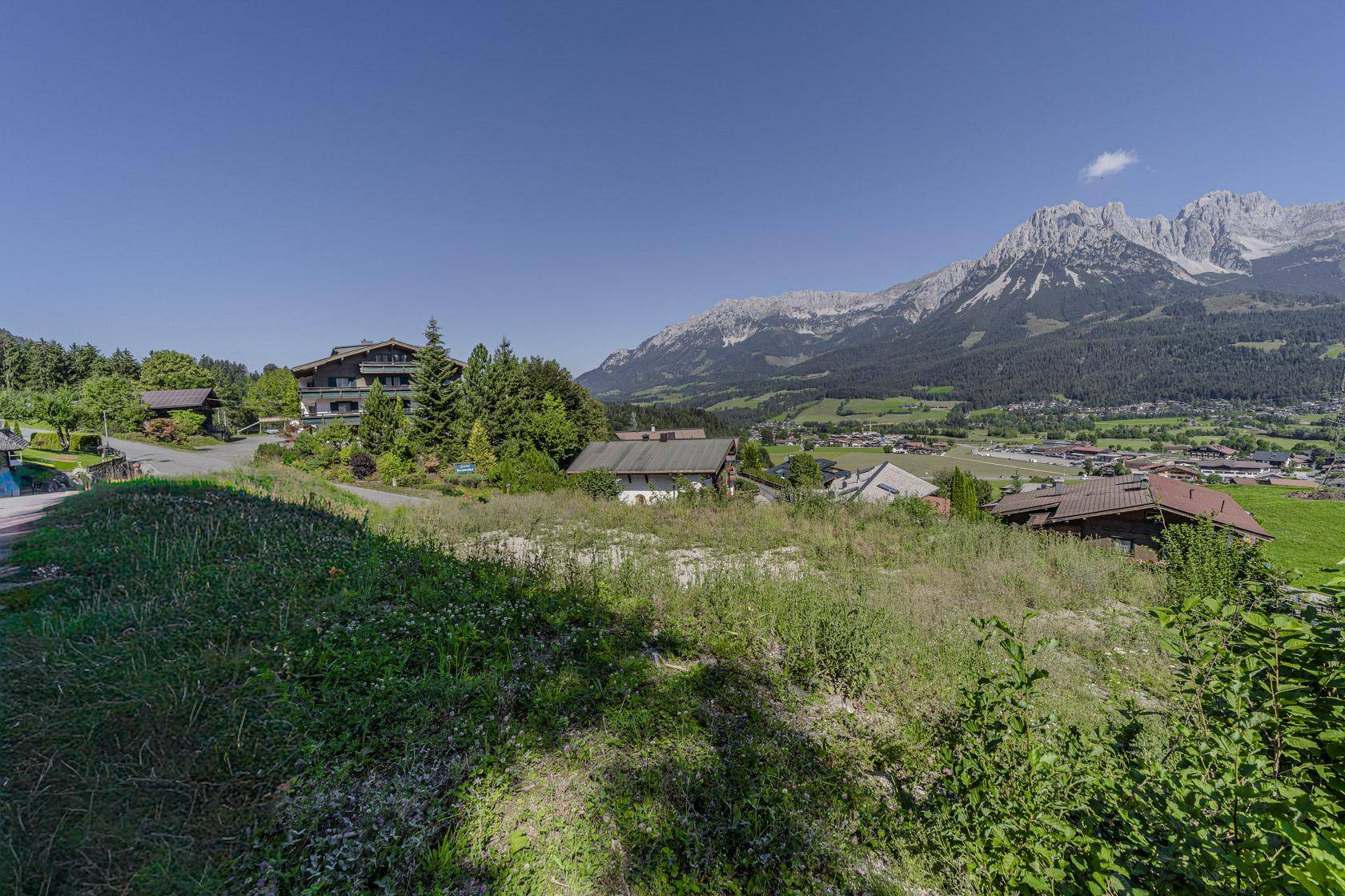 Idyllische Landschaft mit grünen Hügeln, verstreuten Häusern und einer beeindruckenden Bergkulisse.