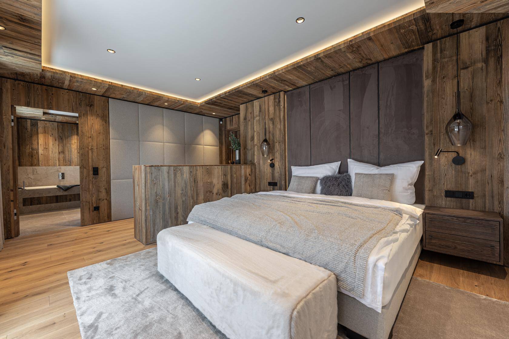 Luxuriöses Schlafzimmer mit Holzwänden, indirekter Beleuchtung und offenem Zugang zum modernen Badezimmer.