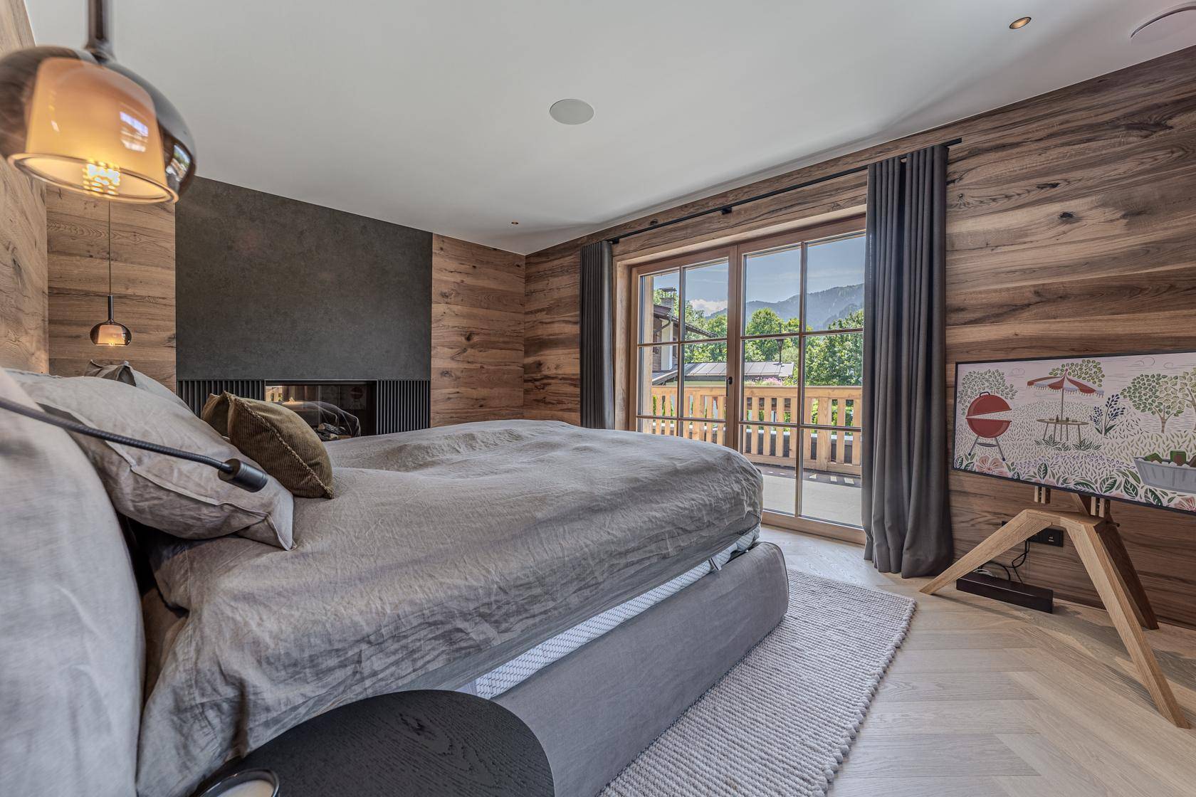 Modernes Schlafzimmer mit Holzwänden, großem Bett und Zugang zu einem Balkon mit Bergblick.