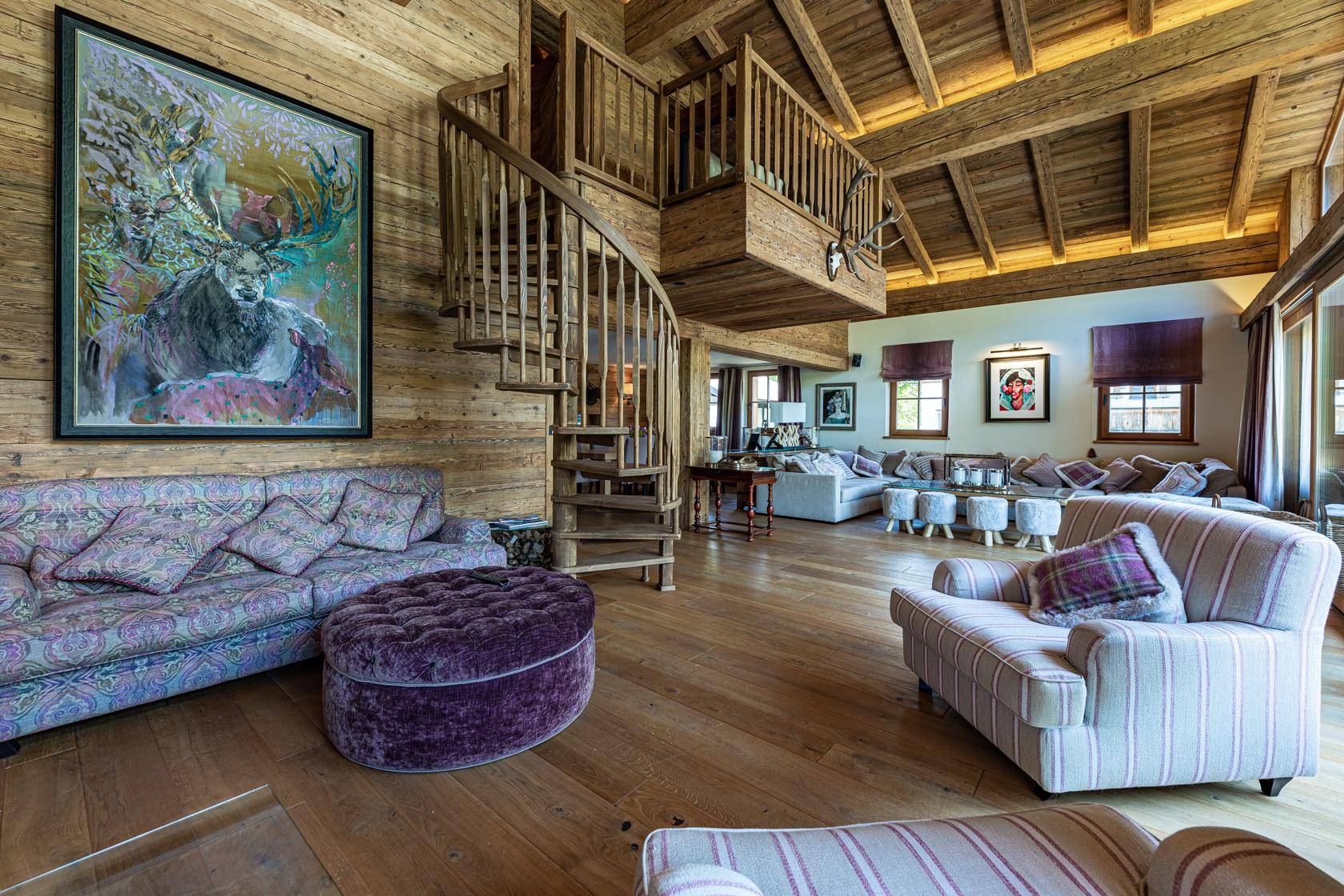 Geräumiges Wohnzimmer mit hohen Holzdecken, Wendeltreppe, großem Sofa und alpiner Kunst.