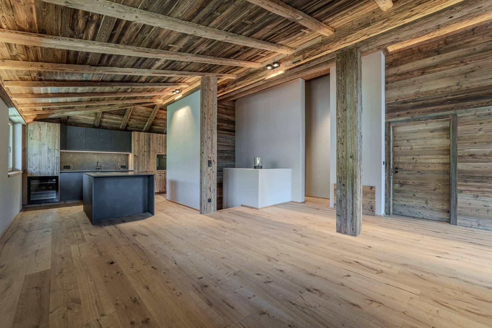 Geräumiger offener Wohnbereich mit Holzbalkendecke, Holzboden und integrierter moderner Küche.