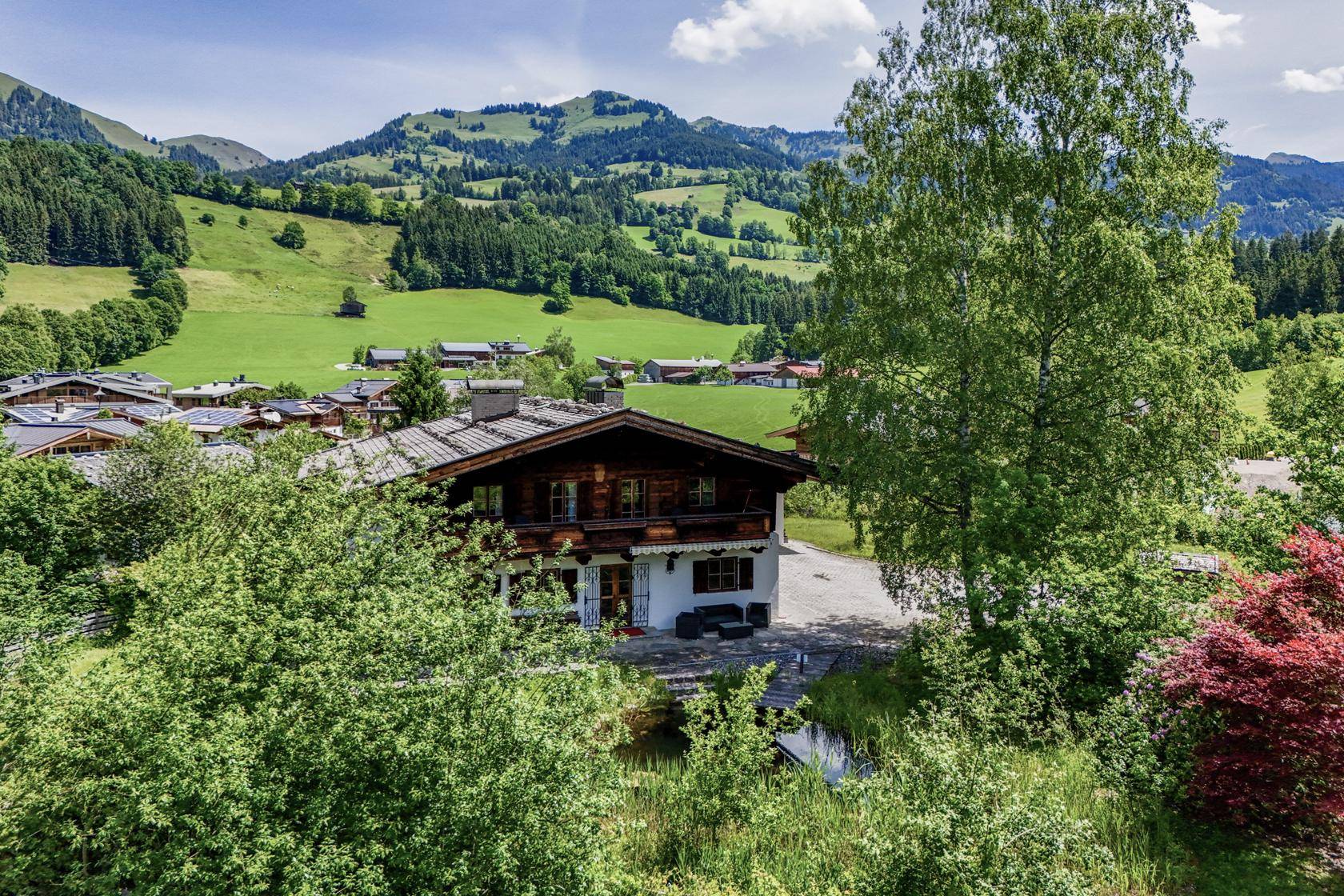 Traditionelles Holzchalet mit Balkon, umgeben von üppiger Natur und Bergblick.