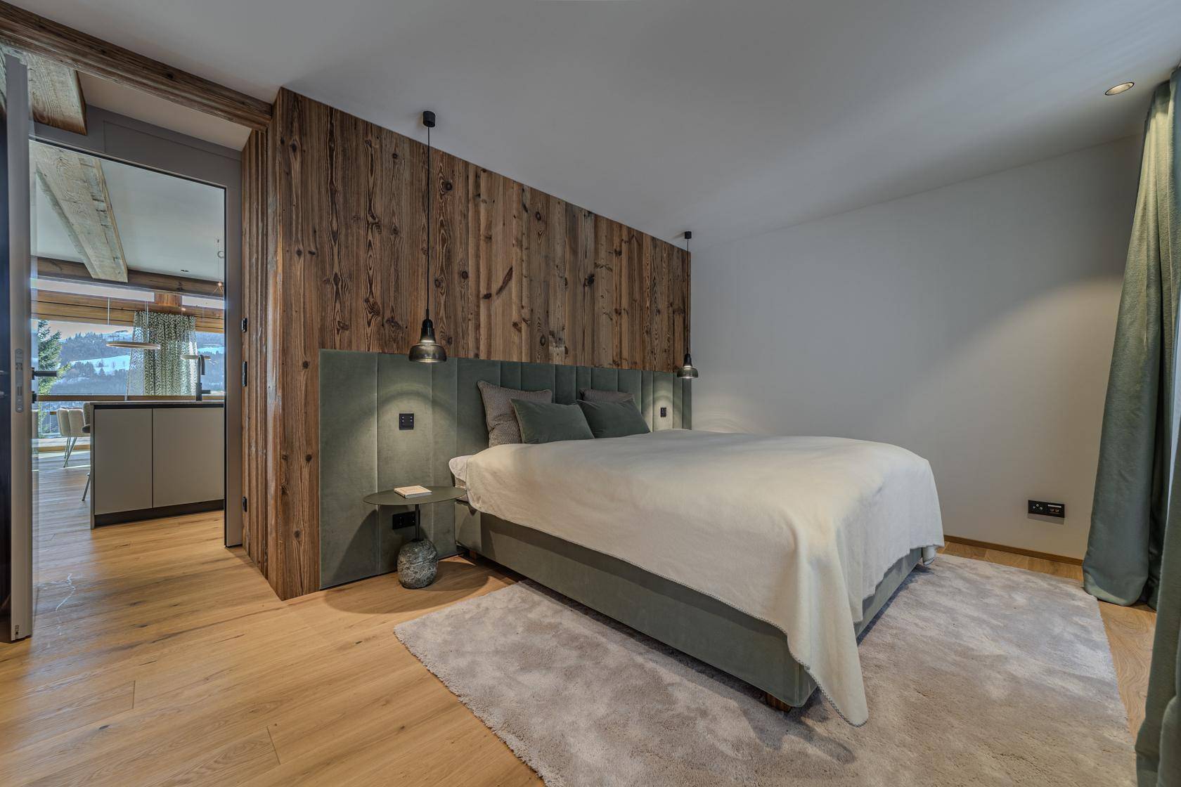Modernes Schlafzimmer mit Holzwand, Doppelbett und Blick in den offenen Wohnbereich.