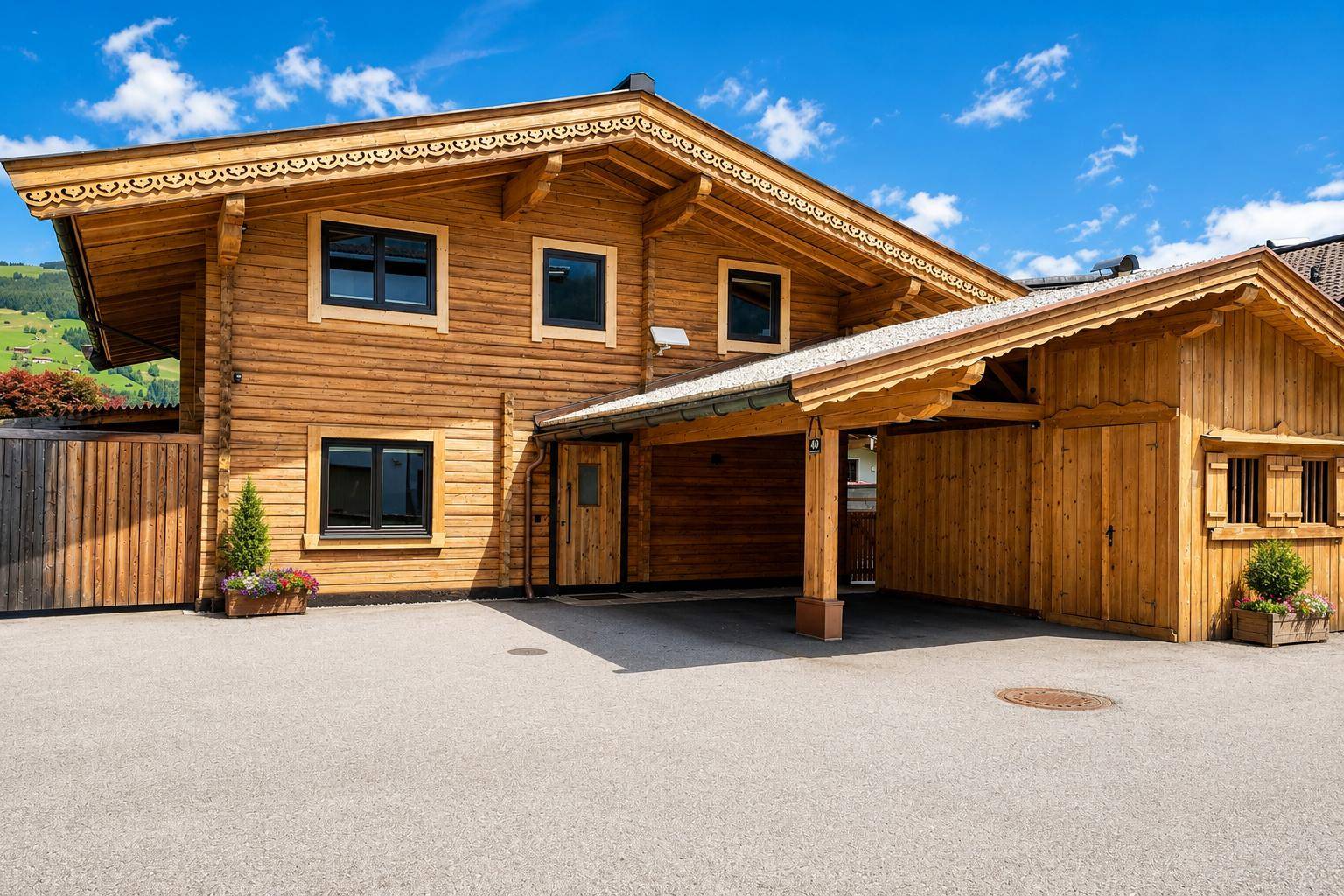 Traditionelles Holzchalet mit Carport und gepflegter Zufahrt unter blauem Himmel.