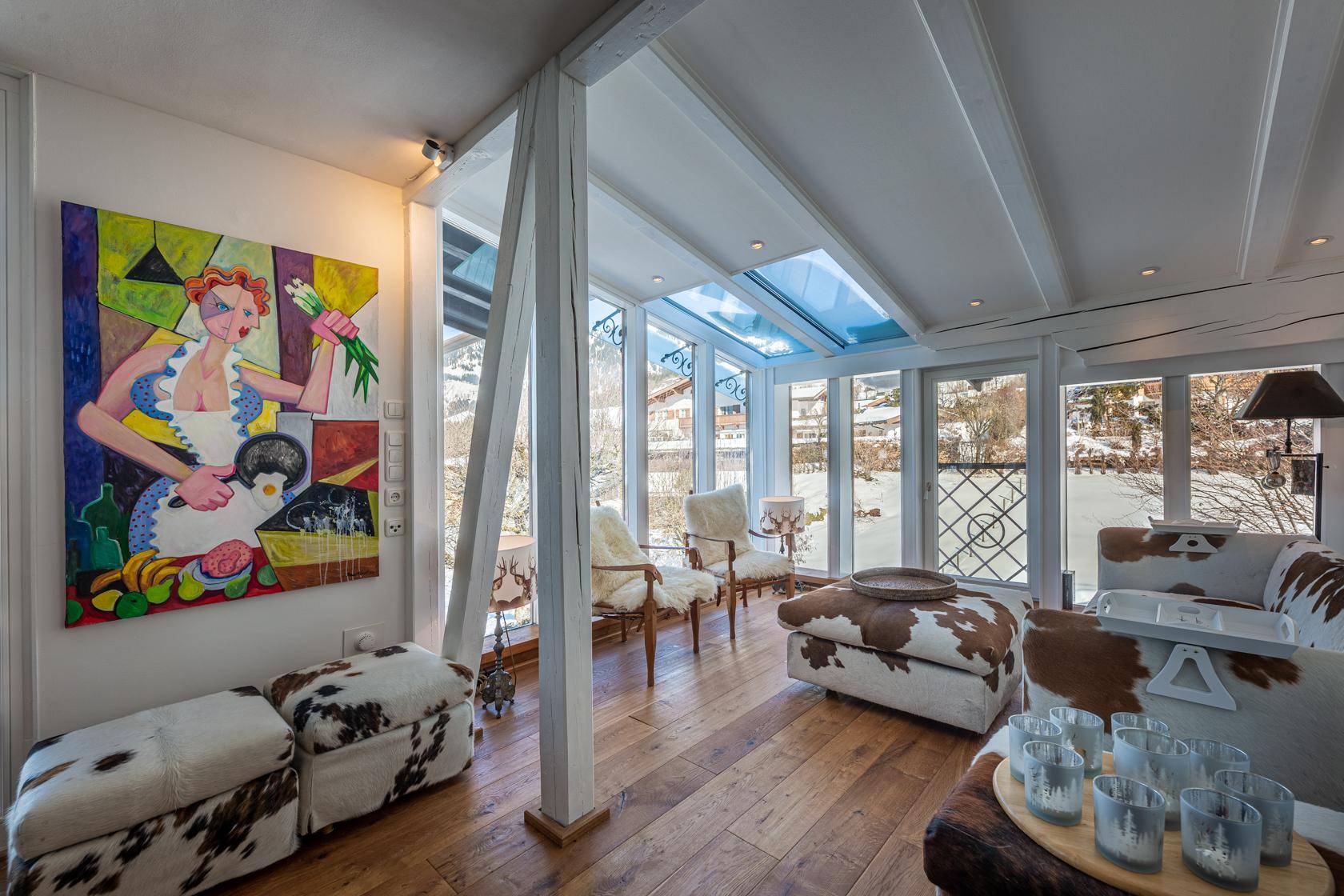 Gemütlicher Wohnbereich mit großen Glasfronten, Bergblick und Kunstwerk an der Wand.