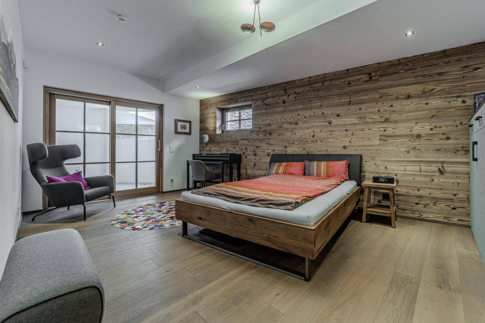 Gemütliches Schlafzimmer mit Holzwand, Doppelbett und Zugang zu einer Terrasse oder Balkon.