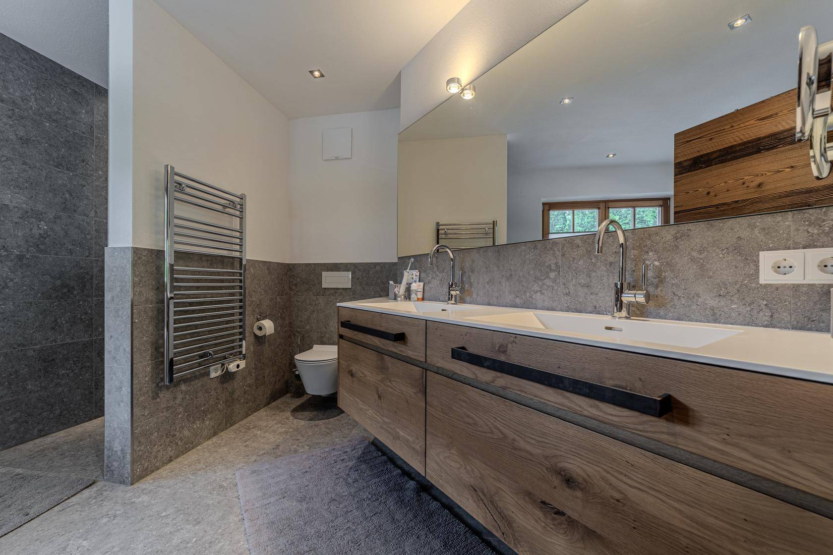 Geräumiges Badezimmer mit Doppelwaschbecken, großer Spiegelfläche und beheiztem Handtuchhalter.