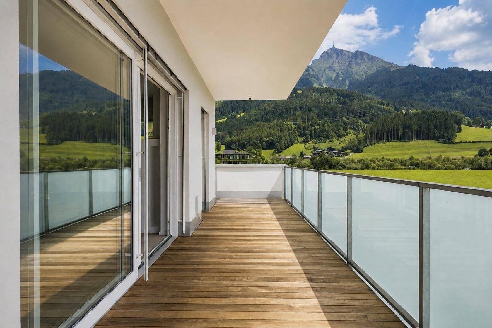 Langer Balkon mit Holzbelag und Glasgeländer, bietet einen weiten Blick auf Berge und Landschaft.