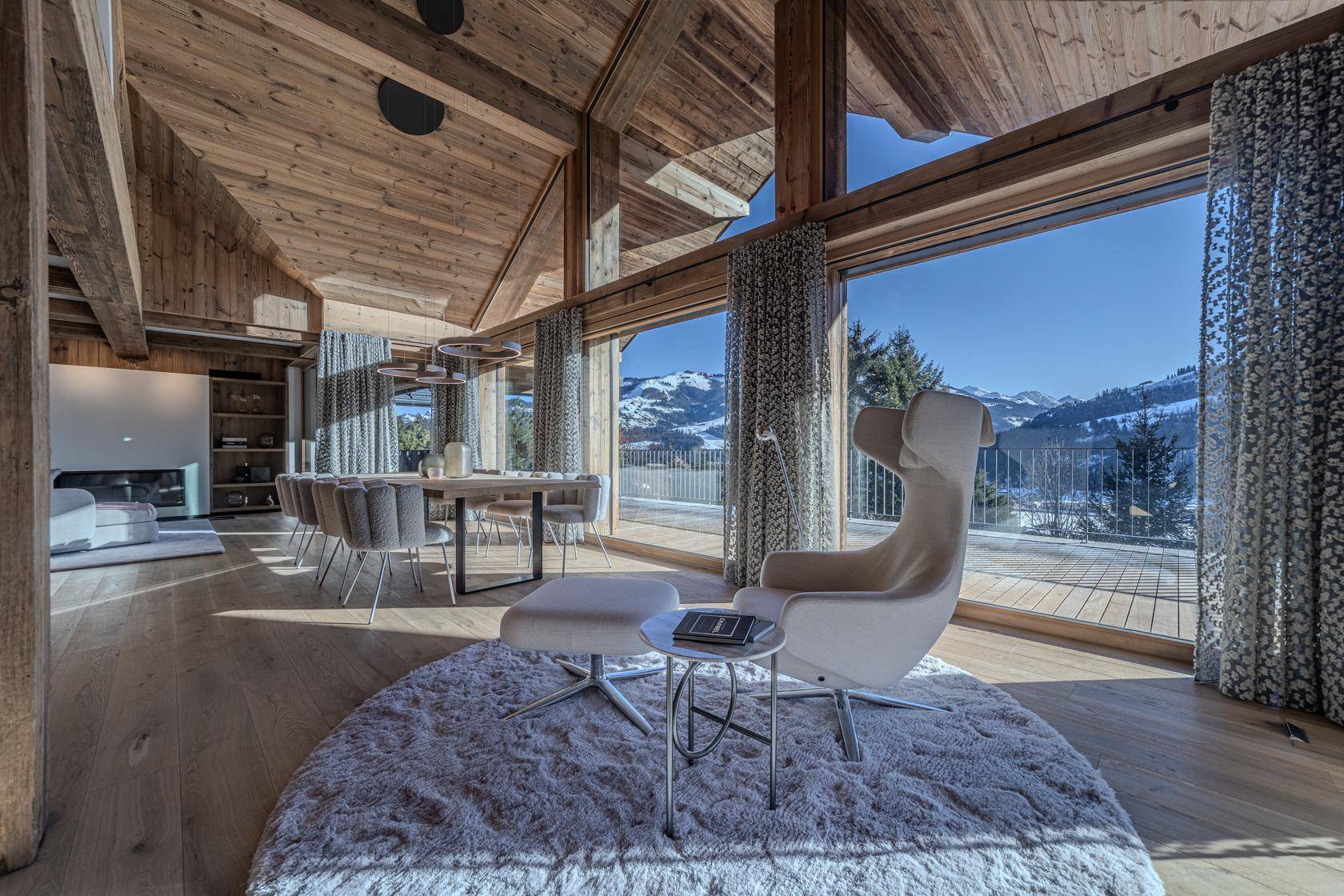 Gemütlicher Wohnbereich mit Sessel, Teppich und weitem Blick auf die verschneite Berglandschaft.