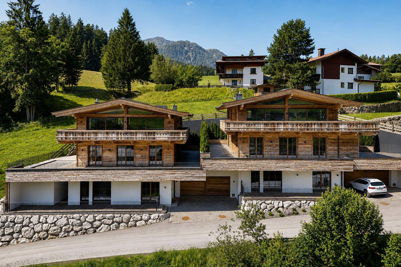 Zwei luxuriöse Chalets mit Holzfassaden und Terrassen, eingebettet in grüne Hügellandschaft.