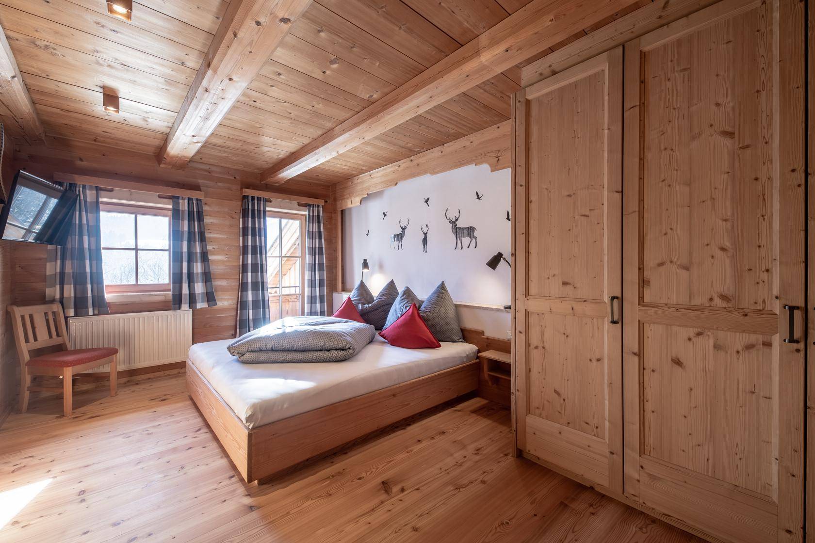Schlafzimmer mit Holzboden, Holzbalkendecke und traditionellen Hirschmotiven an der Wand.