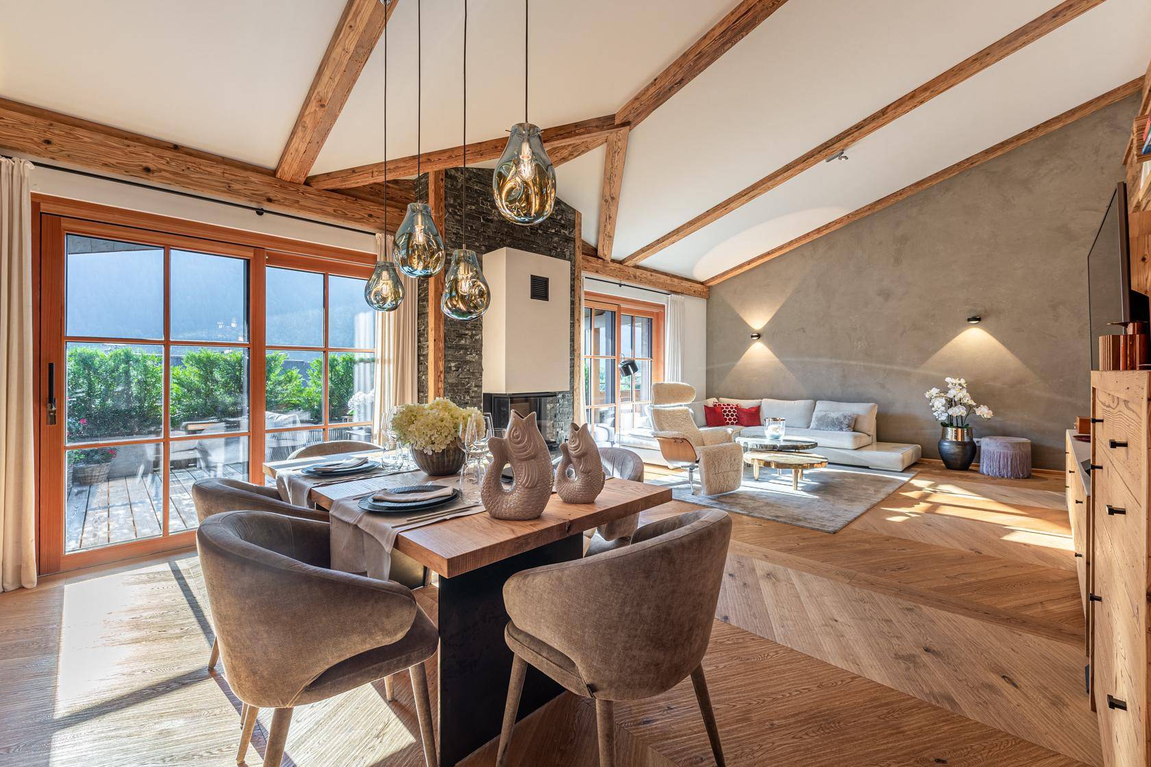 Offener Wohn- und Essbereich mit Holzbalken, Kamin und großen Fenstern zur Terrasse.