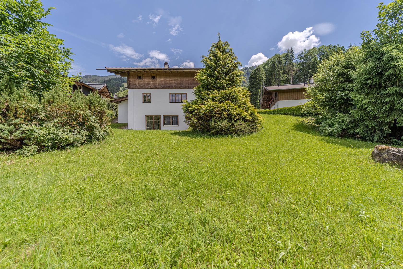 Das Haus ist von einer weitläufigen Rasenfläche und hohen Bäumen umgeben.